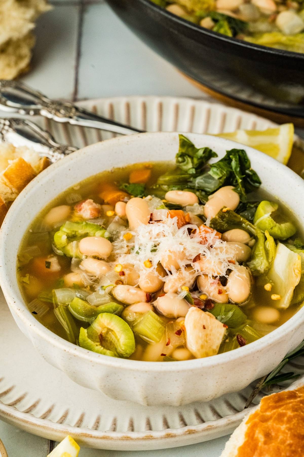 A bowl of white bean and vegetable soup topped with grated cheese and red pepper flakes.