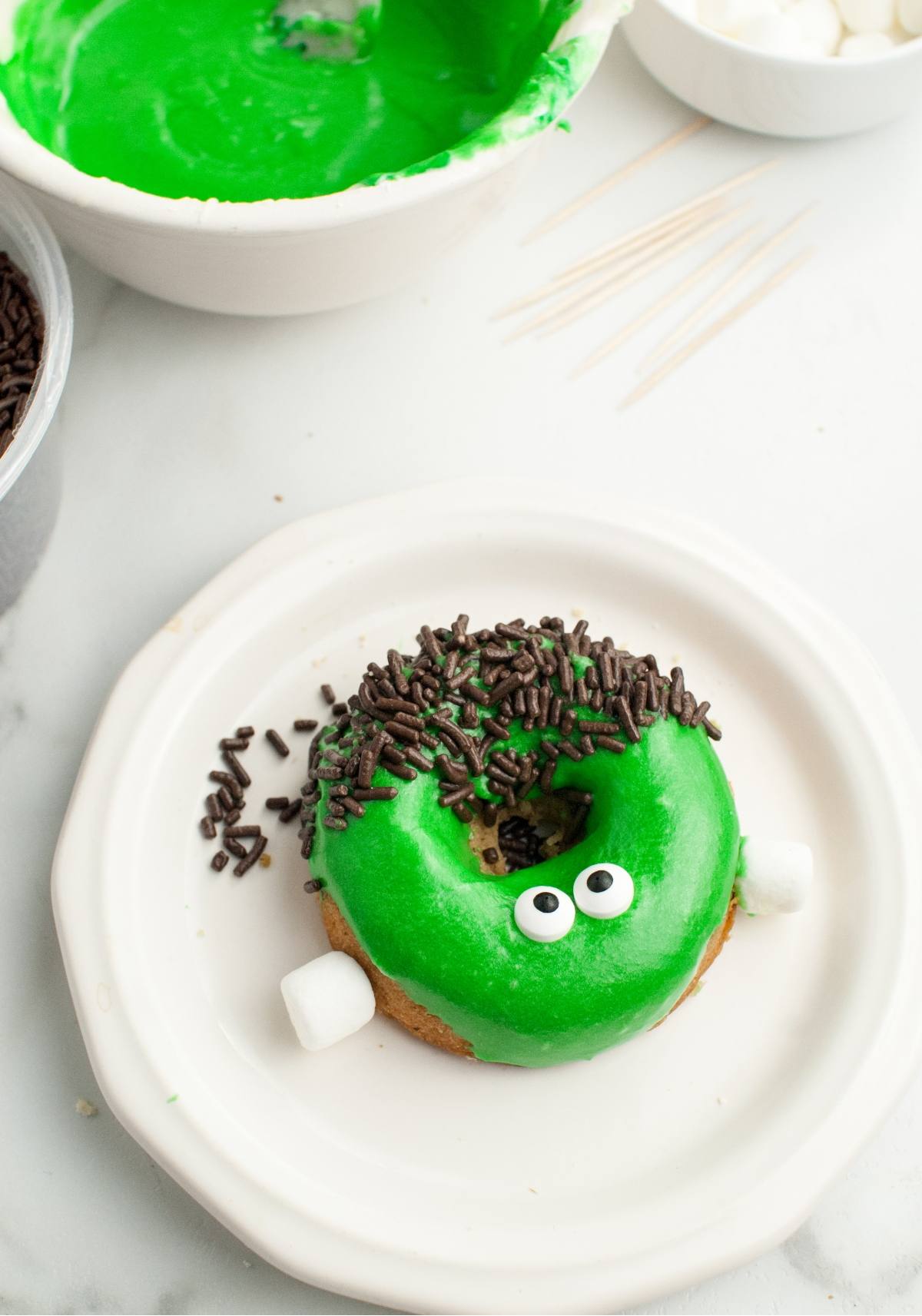 A donut with green icing, candy eyes, chocolate sprinkles, and marshmallows decorated like a monster—perfect for Halloween donut decorating and looks like a Frankenstein monster.