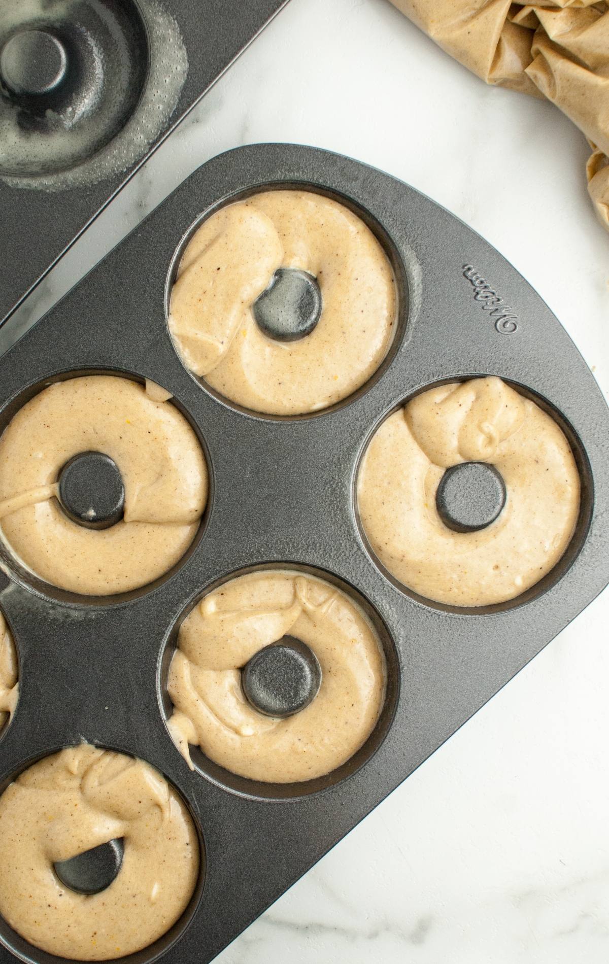 Overhead view of a donut pan filled with raw, light-brown batter, ready to be baked into delicious Frankenstein Apple Cider Halloween Donuts.