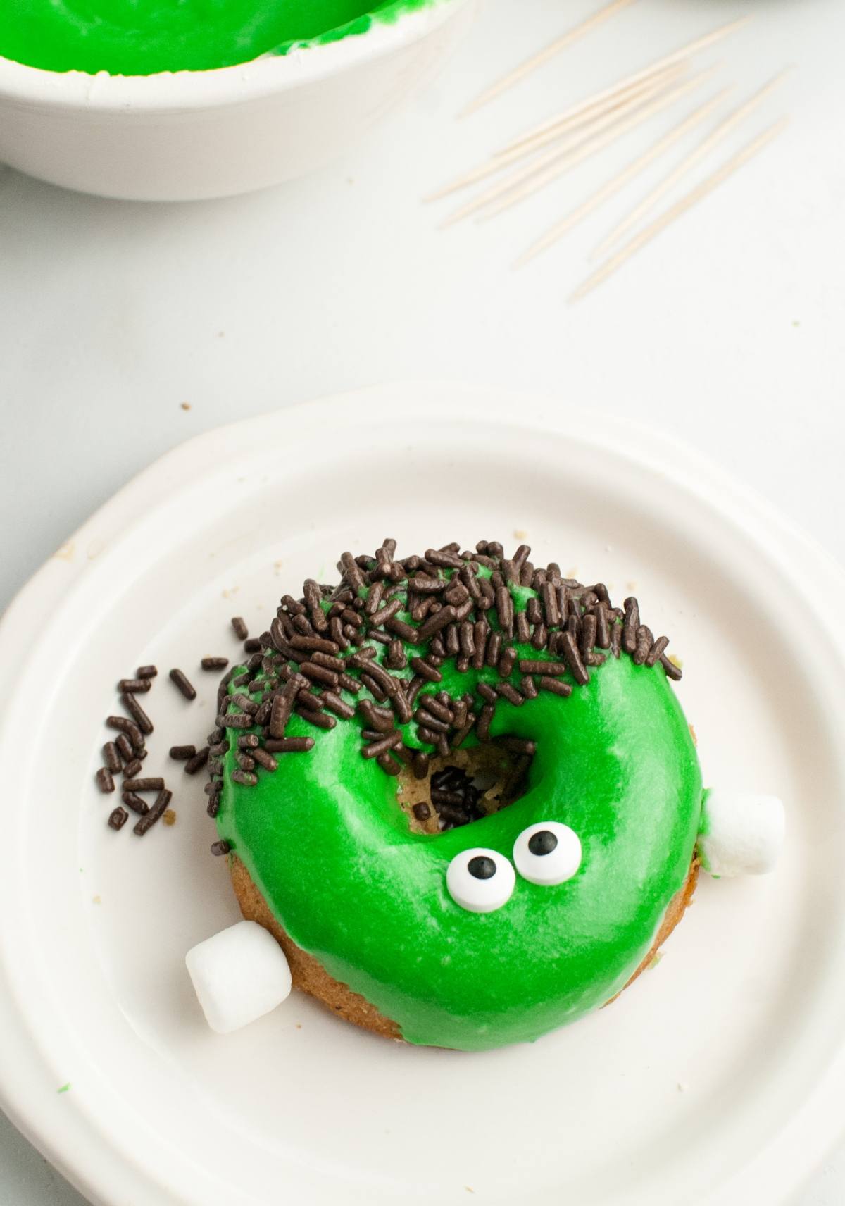 A spooky baked Halloween donut with green icing, candy eyes, chocolate sprinkles, and mini marshmallows—this treat looks like a Frankenstein monster! Perfect for fun Halloween donut decorating.