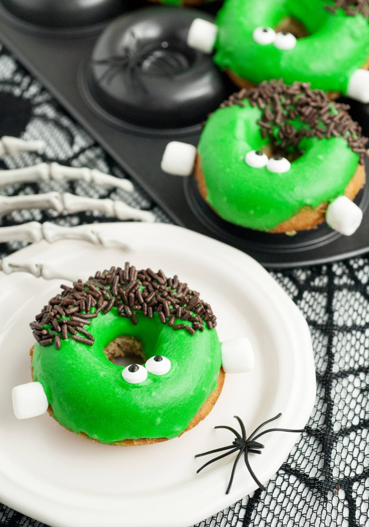 A Halloween donut decorated as Frankenstein with green icing, candy eyes, chocolate sprinkles, and marshmallows for bolts—perfect for spooky Halloween donut decorating or Frankenstein Apple Cider Halloween Donuts.