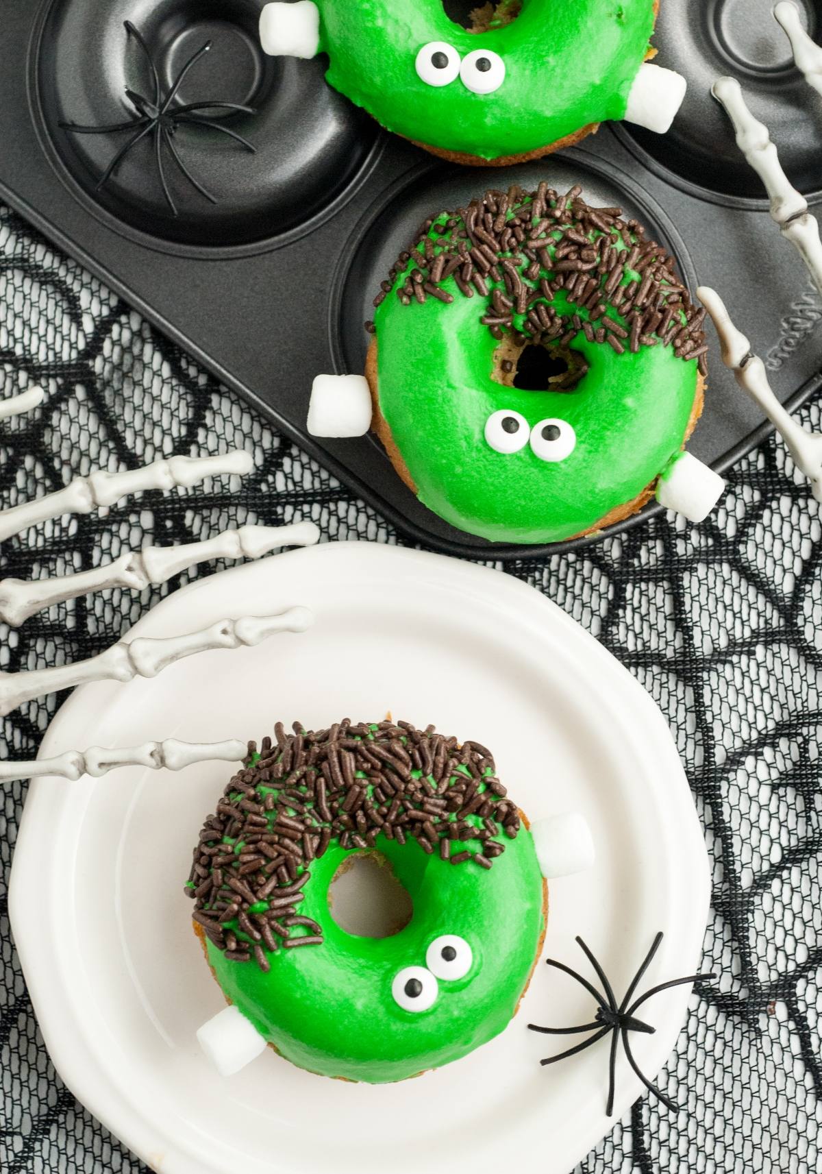 Green monster donuts with candy eyes and chocolate sprinkles, these spooky baked Halloween donuts are styled for Halloween with fake spiders and skeleton hands.