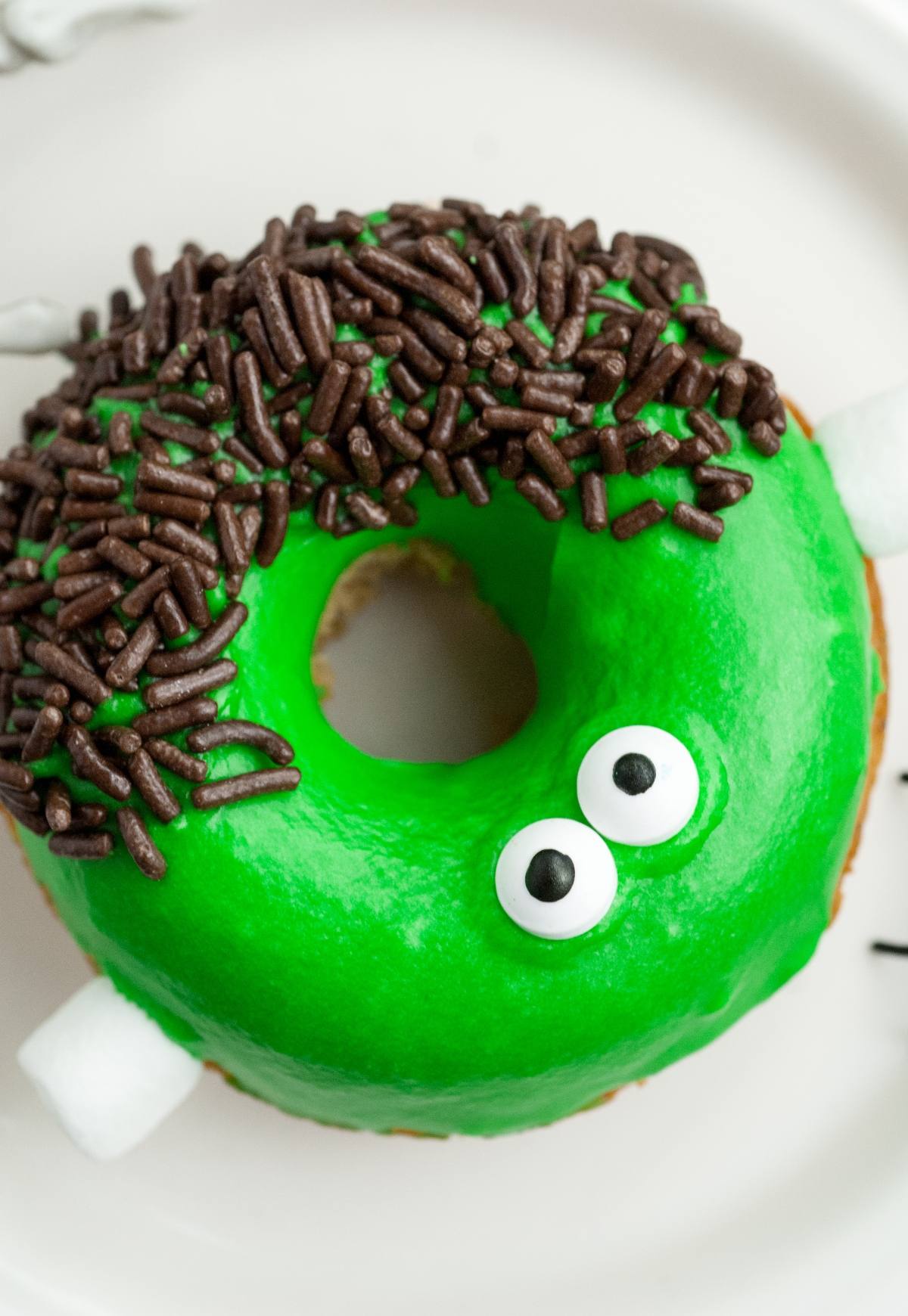 A spooky baked Halloween donut decorated as a green monster with candy eyes, chocolate sprinkles, and marshmallow bolts—perfect for fans of Frankenstein apple cider Halloween donuts!.