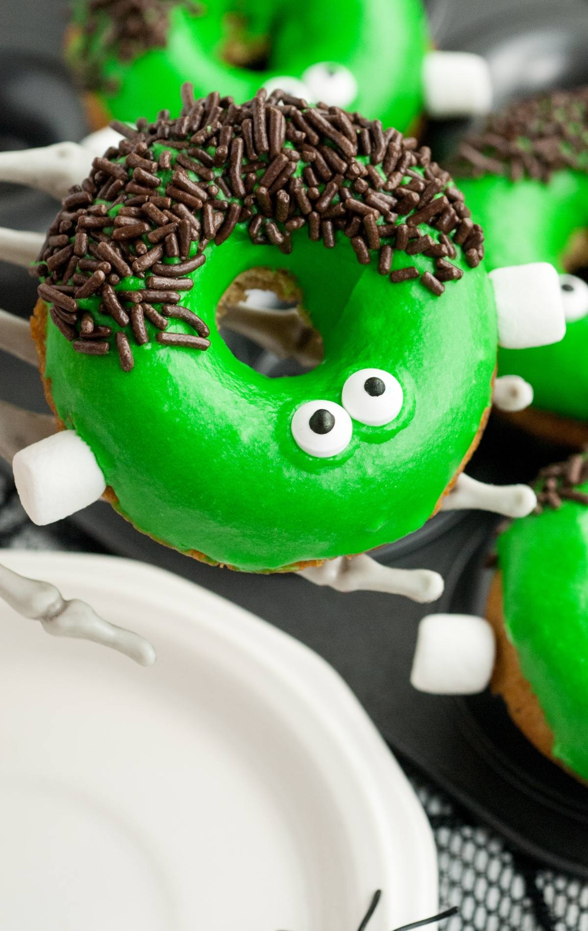 A donut decorated as a green monster with candy eyes, chocolate sprinkles, and marshmallow bolts—this Halloween treat looks like a Frankenstein monster, perfect for Halloween donut decorating!.