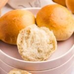 Three soft French bread rolls rest on a plate, one broken open to reveal its fluffy interior.
