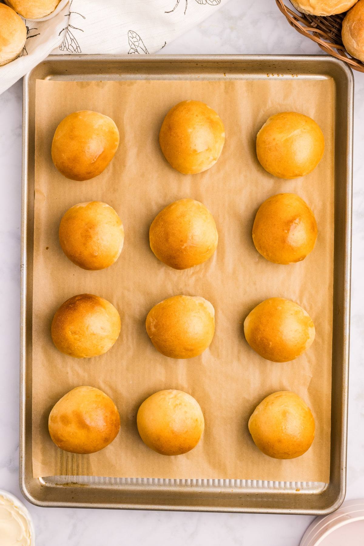 A baking sheet lined with parchment paper holds twelve golden brown dinner rolls.