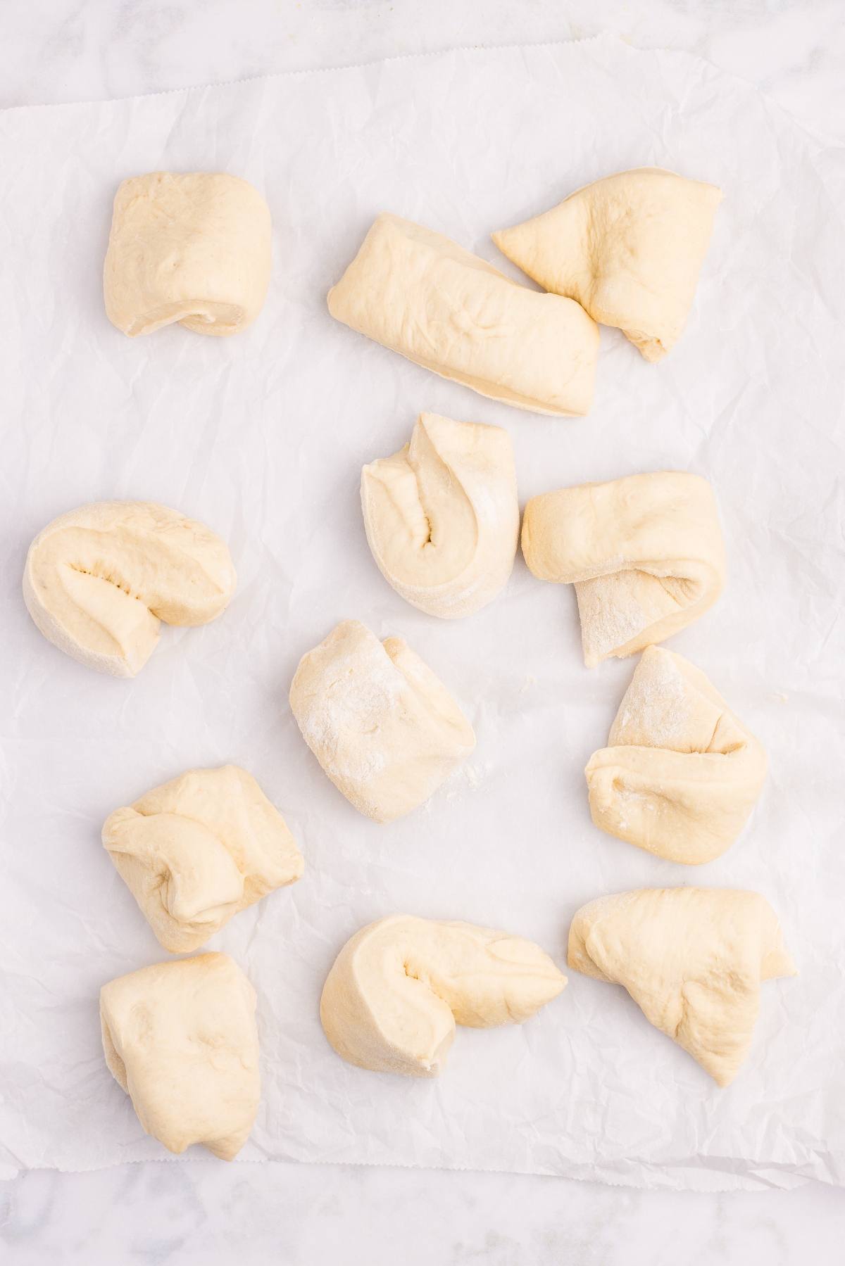 Eleven pieces of raw dough arranged on a sheet of parchment paper.