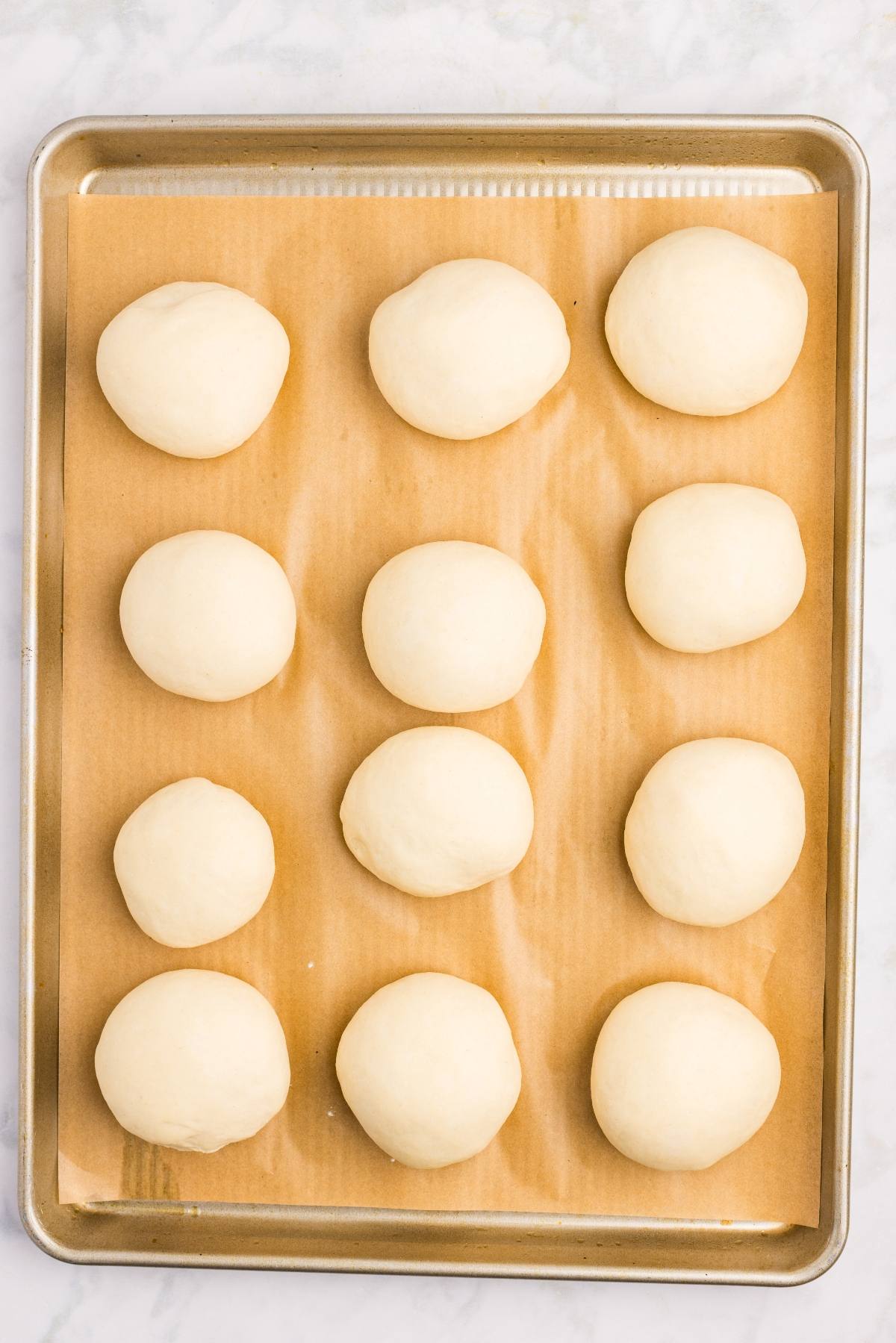 Twelve dough balls evenly spaced on a parchment-lined baking sheet, ready to be baked.