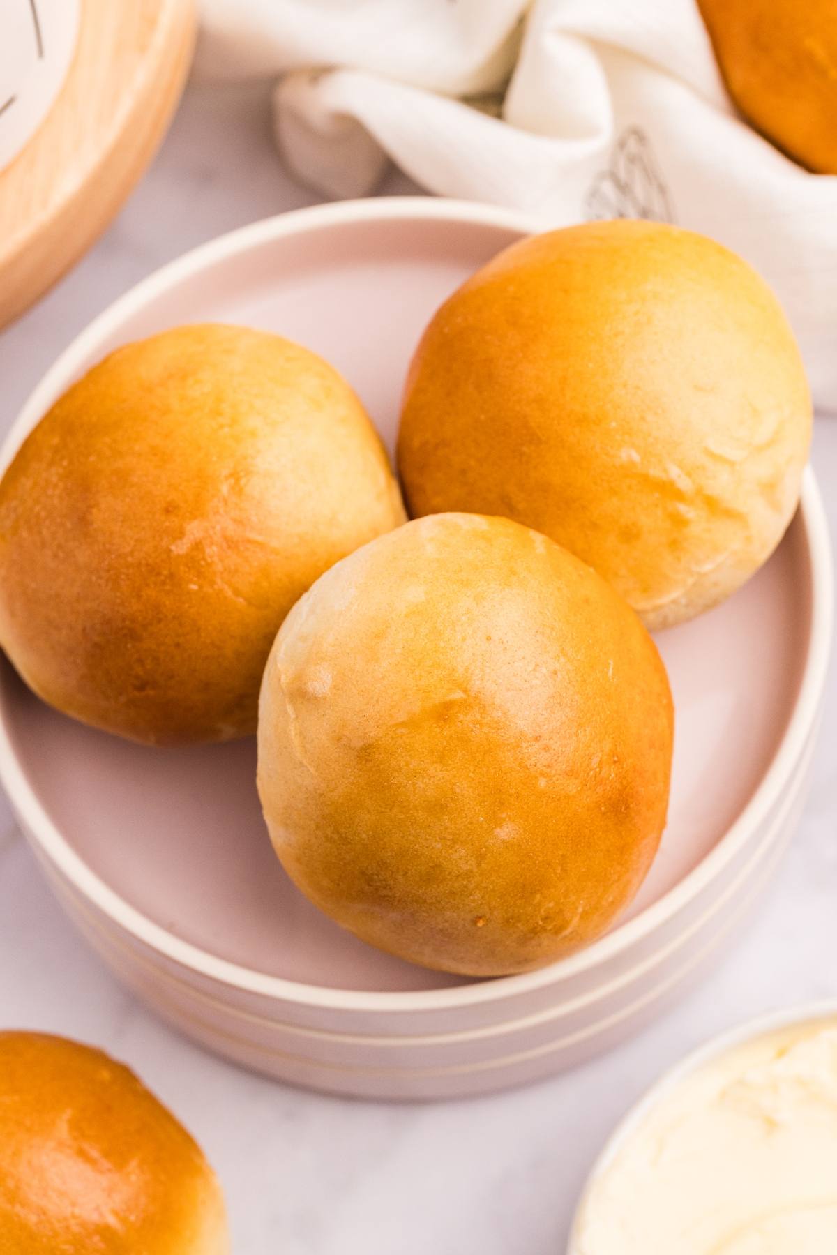 Three golden brown dinner rolls on a pink plate, with a white napkin and butter nearby.