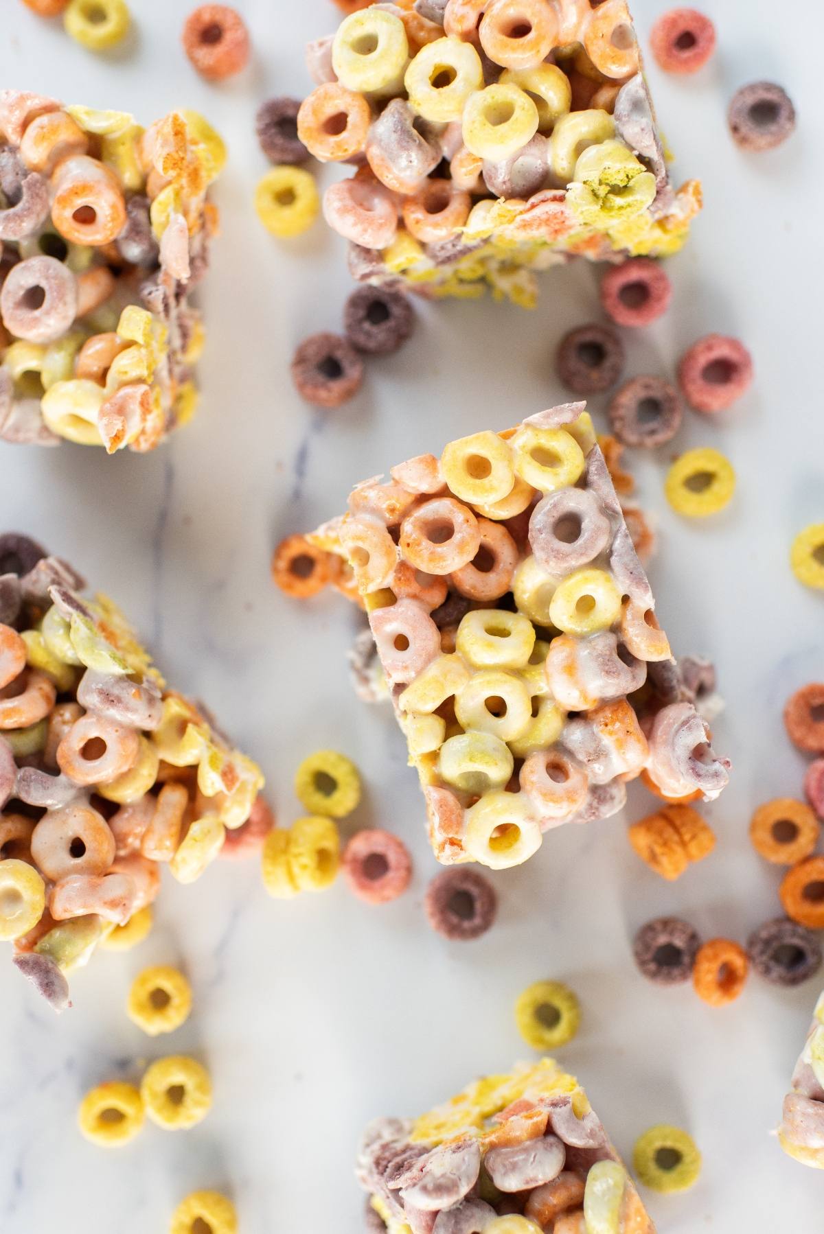 Colorful fruit loops squares with scattered cereal pieces rest on a white marble surface.