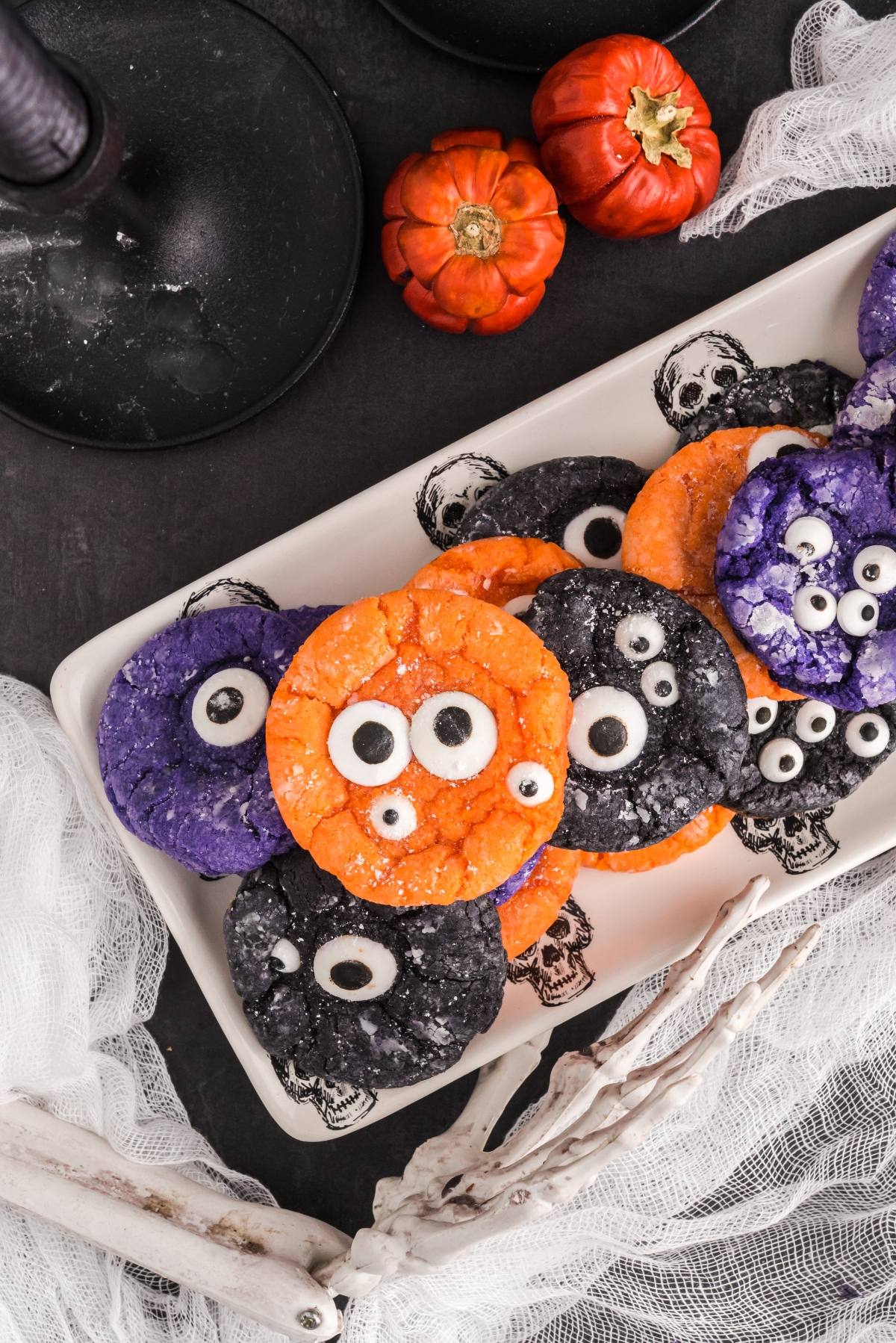 Colorful Cake mix Halloween cookies with candy eyes on a white tray, surrounded by small pumpkins and spooky decor&mdash;perfect for easy Halloween cookie decorating ideas and fun, spooky Halloween treats.