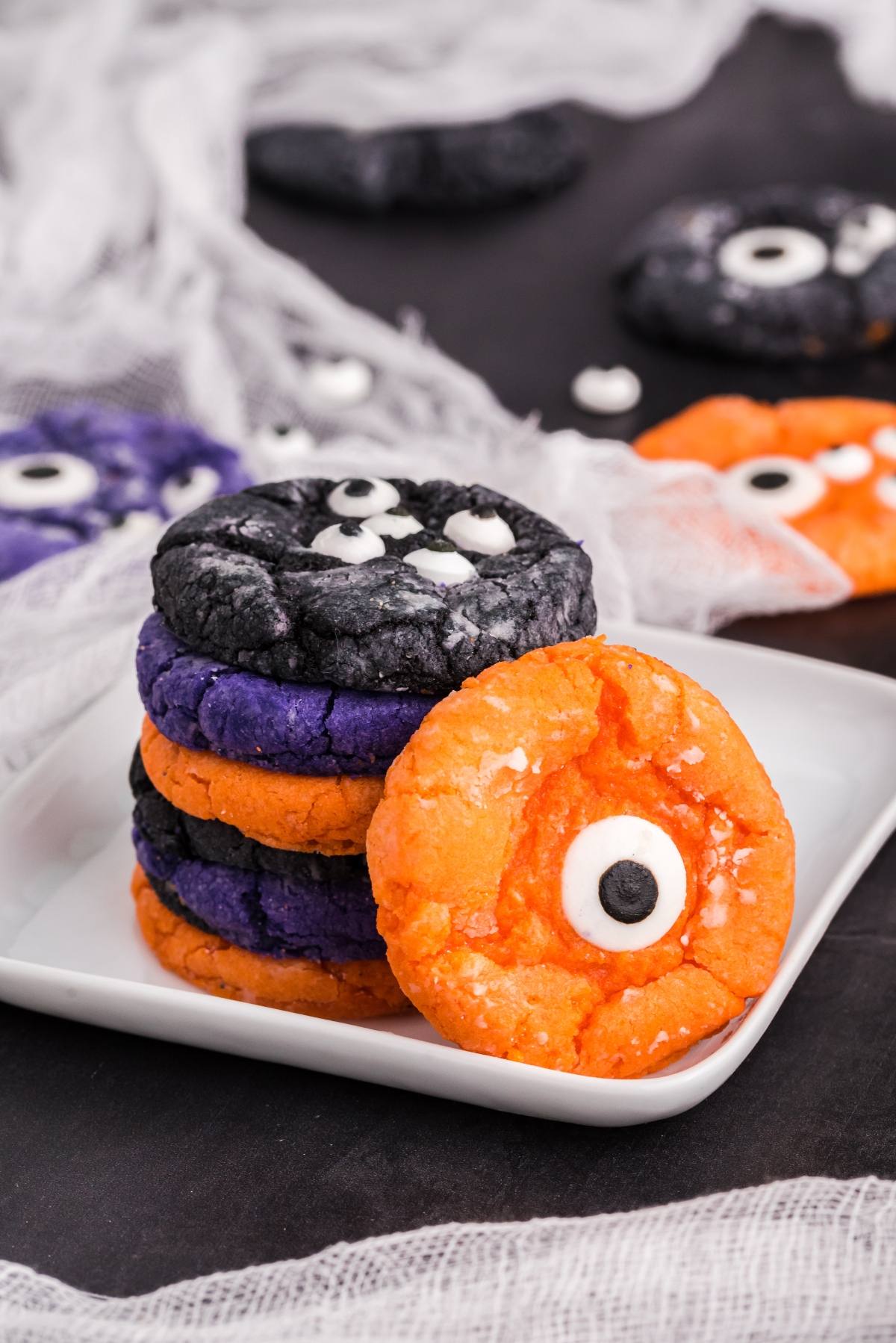 A stack of colourful monster cookies made from cake mix Halloween cookies, topped with candy eyeballs, sits on a white plate&mdash;perfect for easy Halloween cookie decorating ideas.