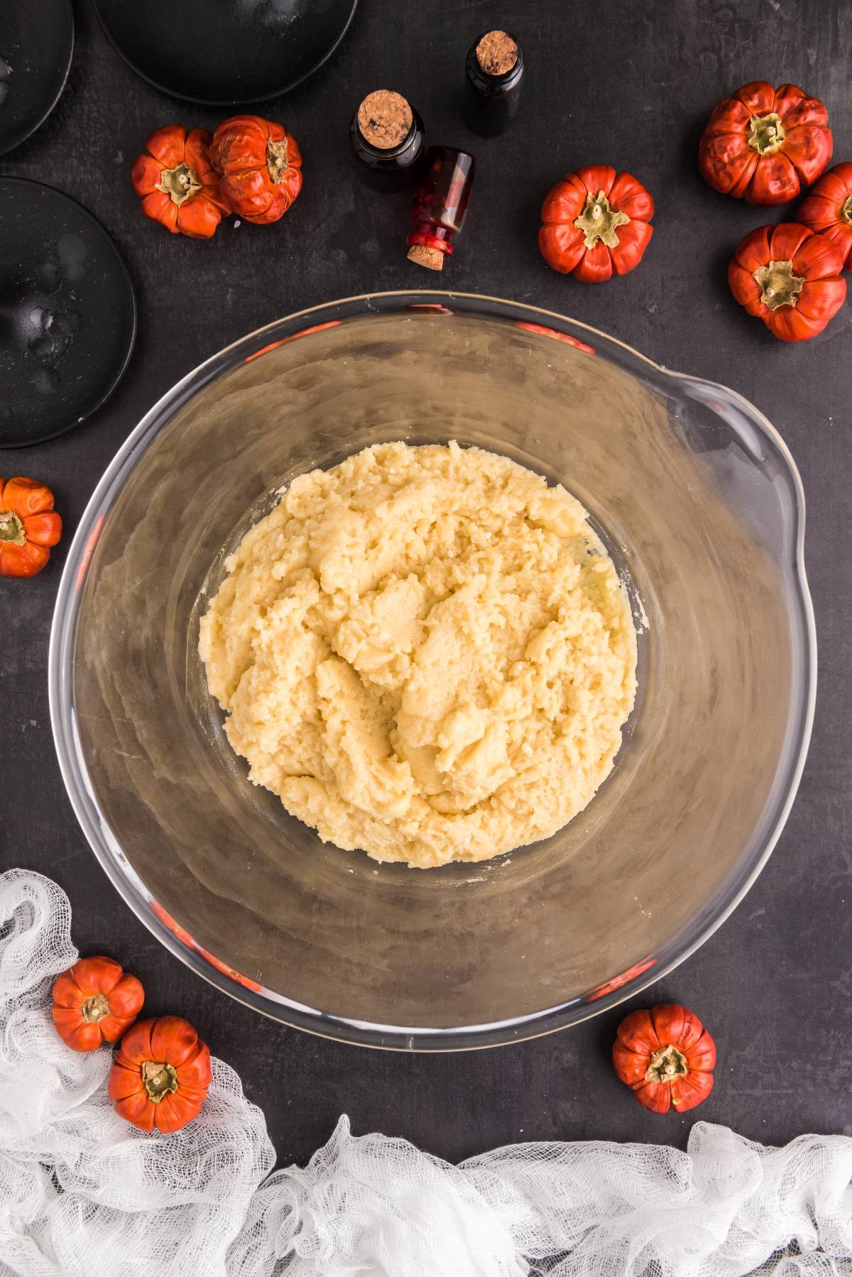 Glass bowl with cookie dough, perfect for Halloween Crinkle Cookies, surrounded by small pumpkins, bottles, and black plates&mdash;ideal setup for easy Halloween cookie decorating ideas and creating spooky Halloween treats.