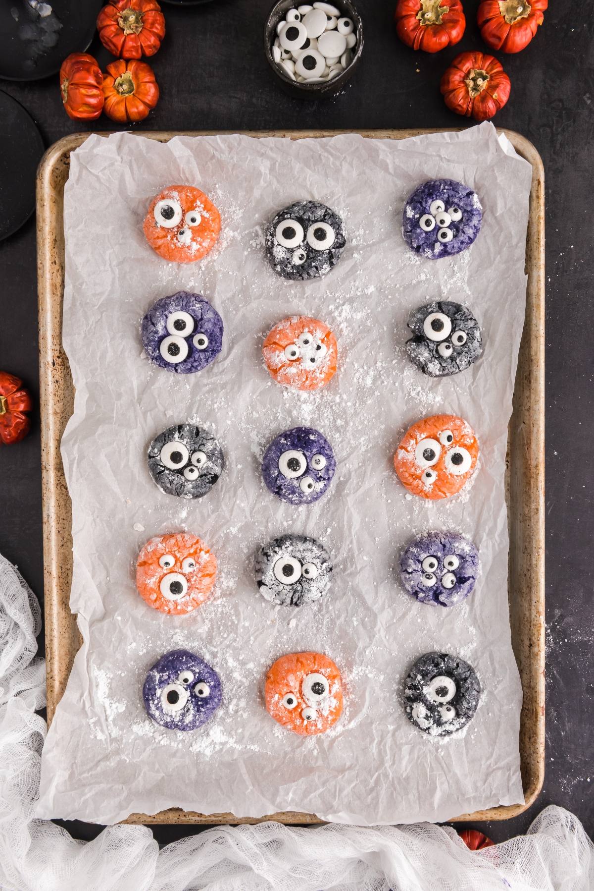 Colorful Halloween mochi with candy eyes on a parchment-lined tray, surrounded by mini pumpkins&mdash;perfect for spooky Halloween treats and easy Halloween cookie decorating ideas.