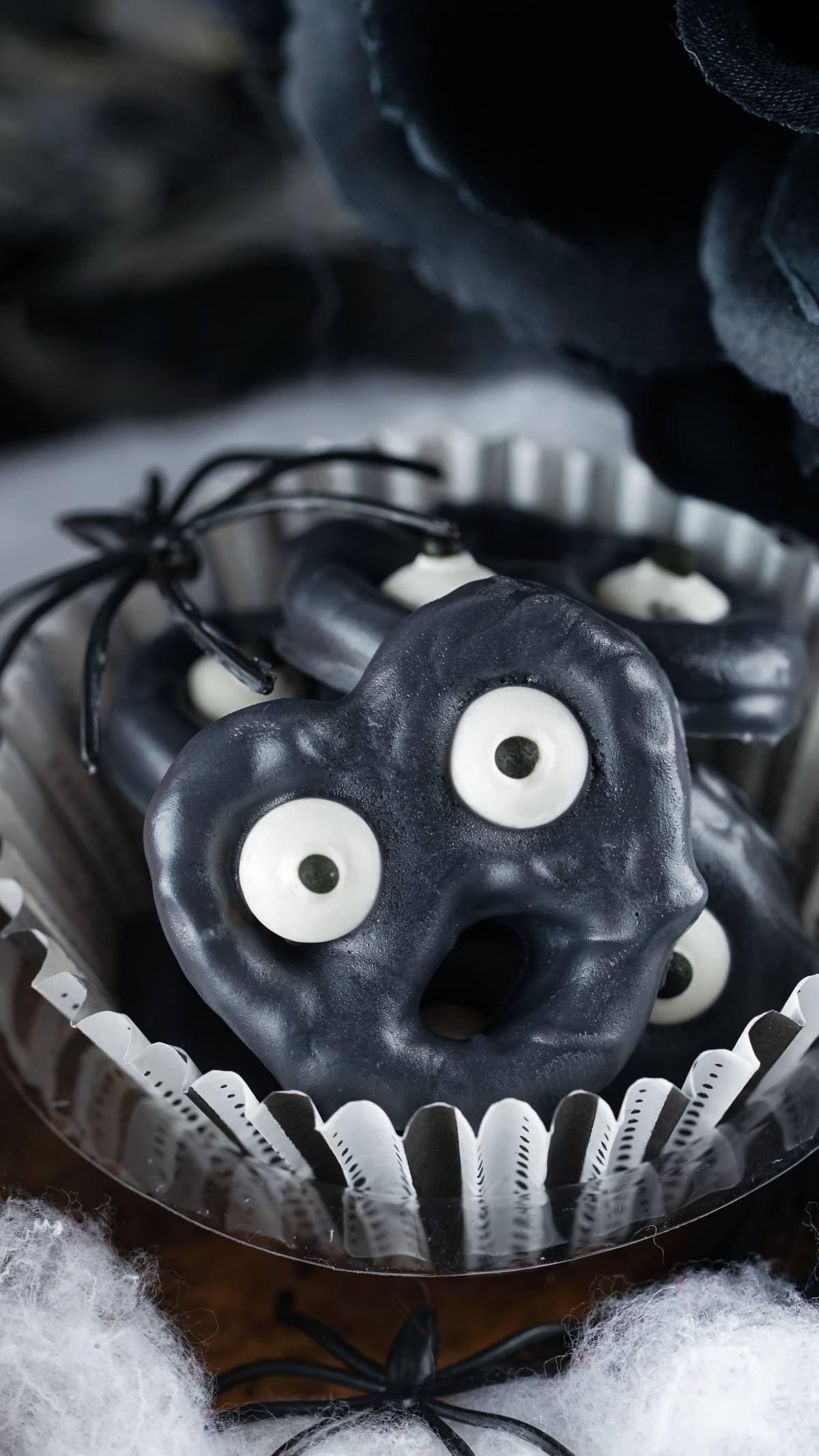 Black Halloween pretzels with eyeballs and open mouths, arranged in a silver cupcake liner—an easy party treat recipe that's the perfect Halloween snack for kids.