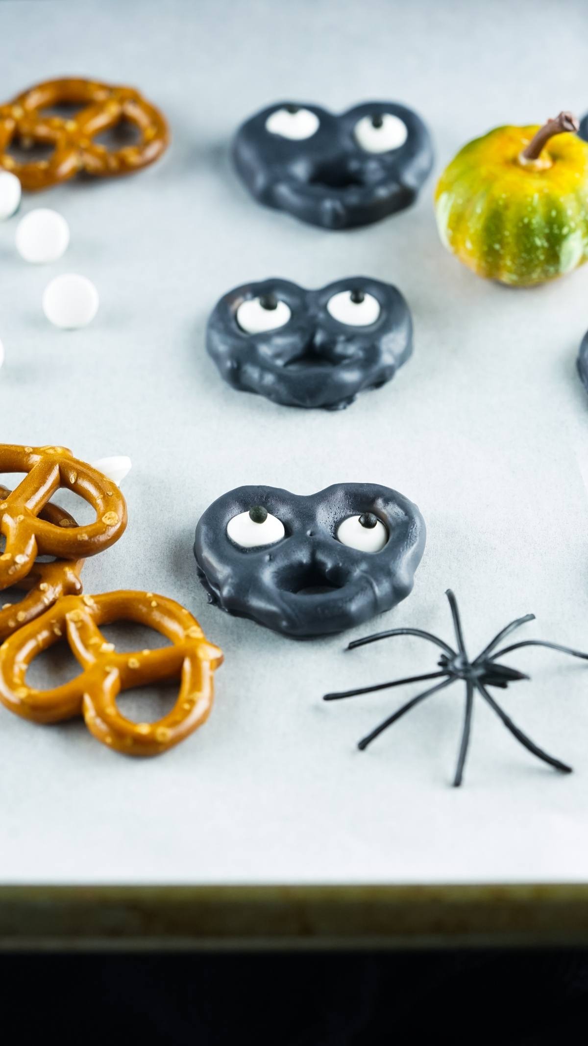 Chocolate-dipped Halloween pretzels with eyeballs, a fake spider, and a small gourd make an easy party treat recipe perfect for a fun Halloween snack for kids.