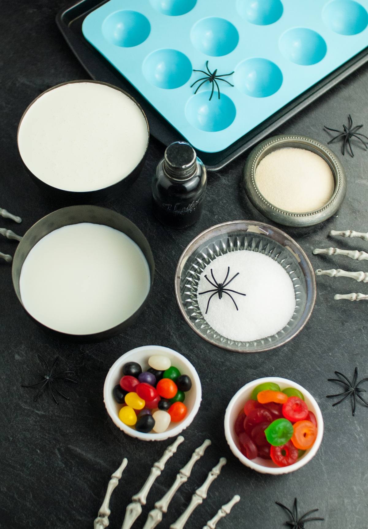 Jelly, gummy candy, sugar, cream, milk, gelatin, and black food coloring come together for Halloween Panna Cotta Eyeballs—a dessert that looks like eyeballs surrounded by spooky Halloween props on a table.