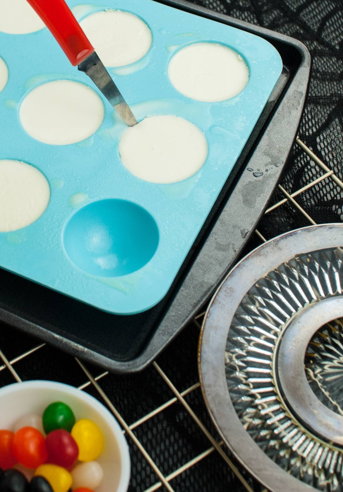 A knife cuts into white batter in a blue silicone mold on a tray, with candy and a metal tool nearby—perfect for a gluten free Halloween dessert or creepy dessert that looks like eyeballs.