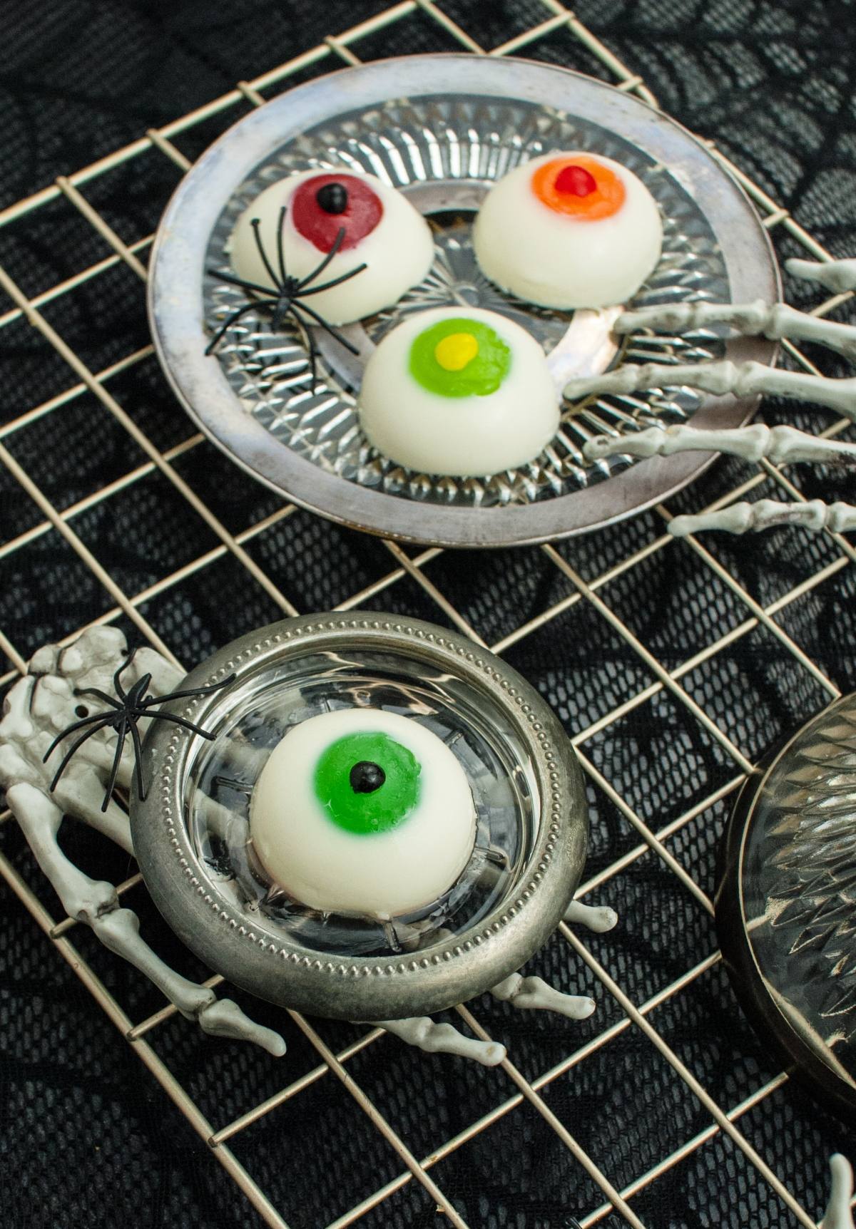 Round gluten free Halloween desserts decorated as eyeballs on silver plates with fake spiders and skeleton hands—a deliciously gross looking Halloween food perfect for spooky parties.