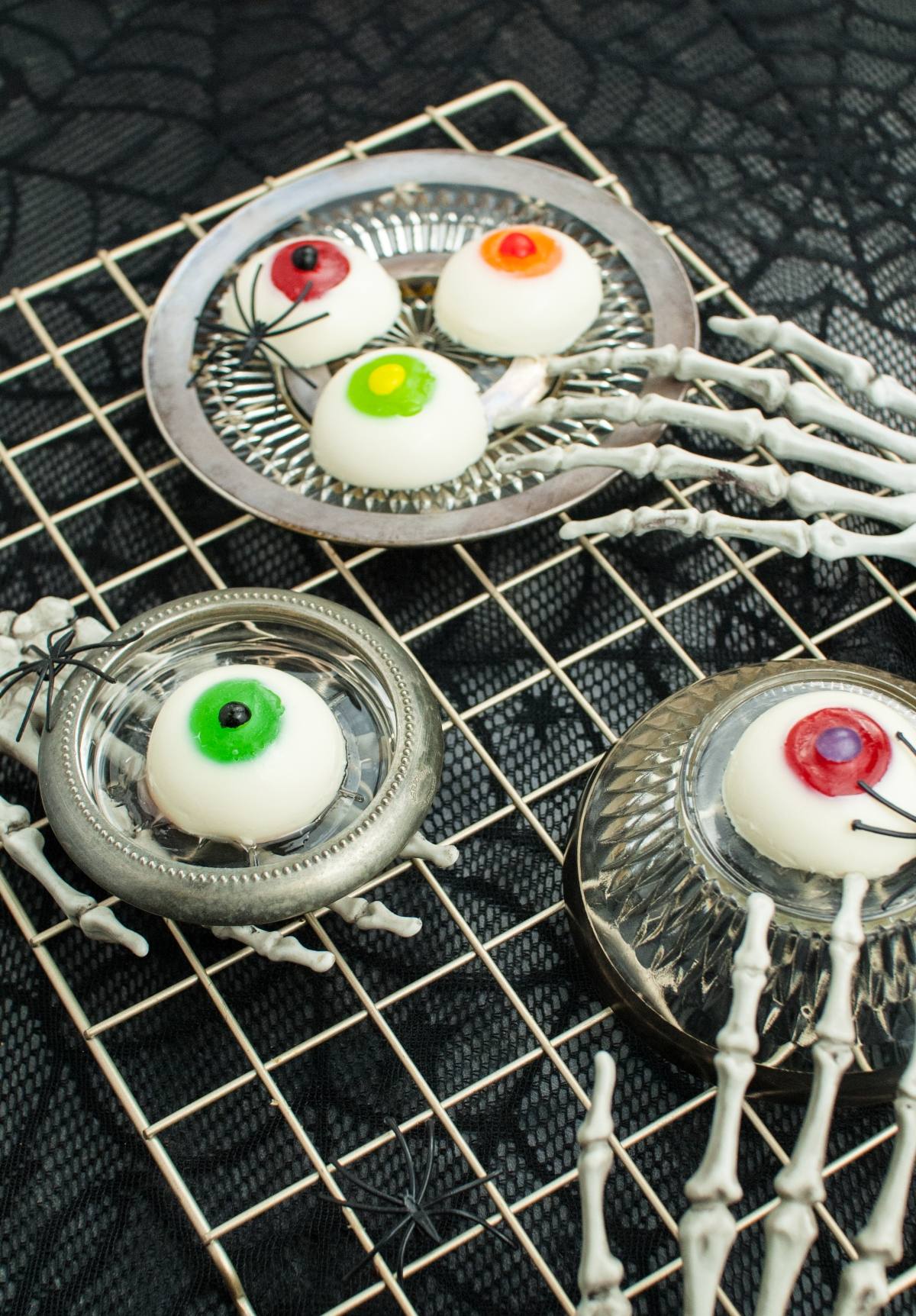Halloween Panna Cotta Eyeballs served on silver dishes, held by skeleton hands on a wire rack—perfect for your collection of gross looking Halloween food and unique Halloween party food ideas.