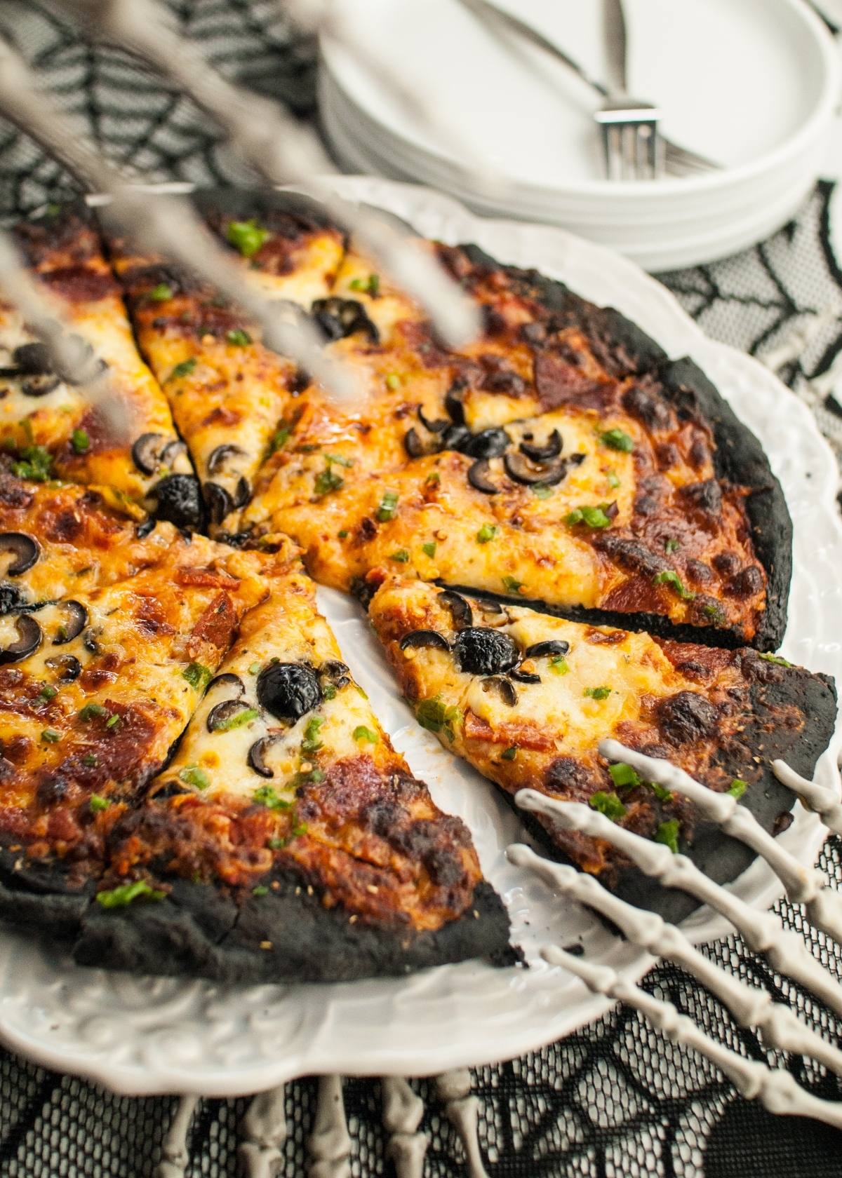 Skeleton hands grabbing slices of black crust pizza—with cheese and olives atop charcoal pizza dough—make a spooky addition to your Halloween dinner menu for adults and kids.