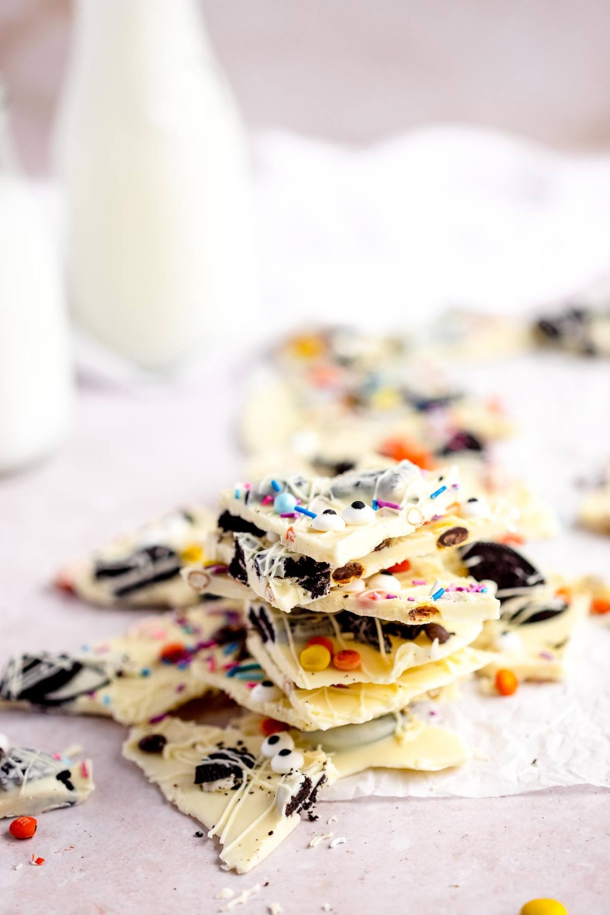 A stack of white chocolate bark with colorful candies and cookie pieces, perfect as an easy candy bark recipe for DIY Halloween candy, with milk bottles in the background.