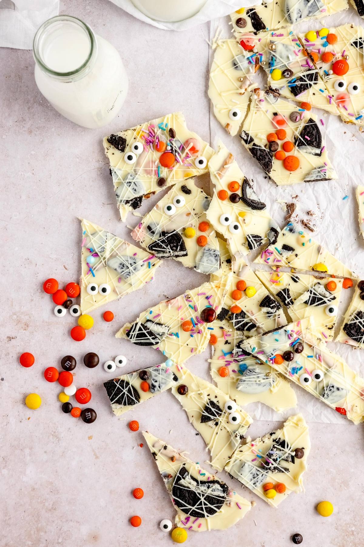 DIY Halloween candy: White Chocolate Bark with googly monster eyes, colorful sprinkles, and candies, served next to a bottle of milk for a fun Halloween treat.