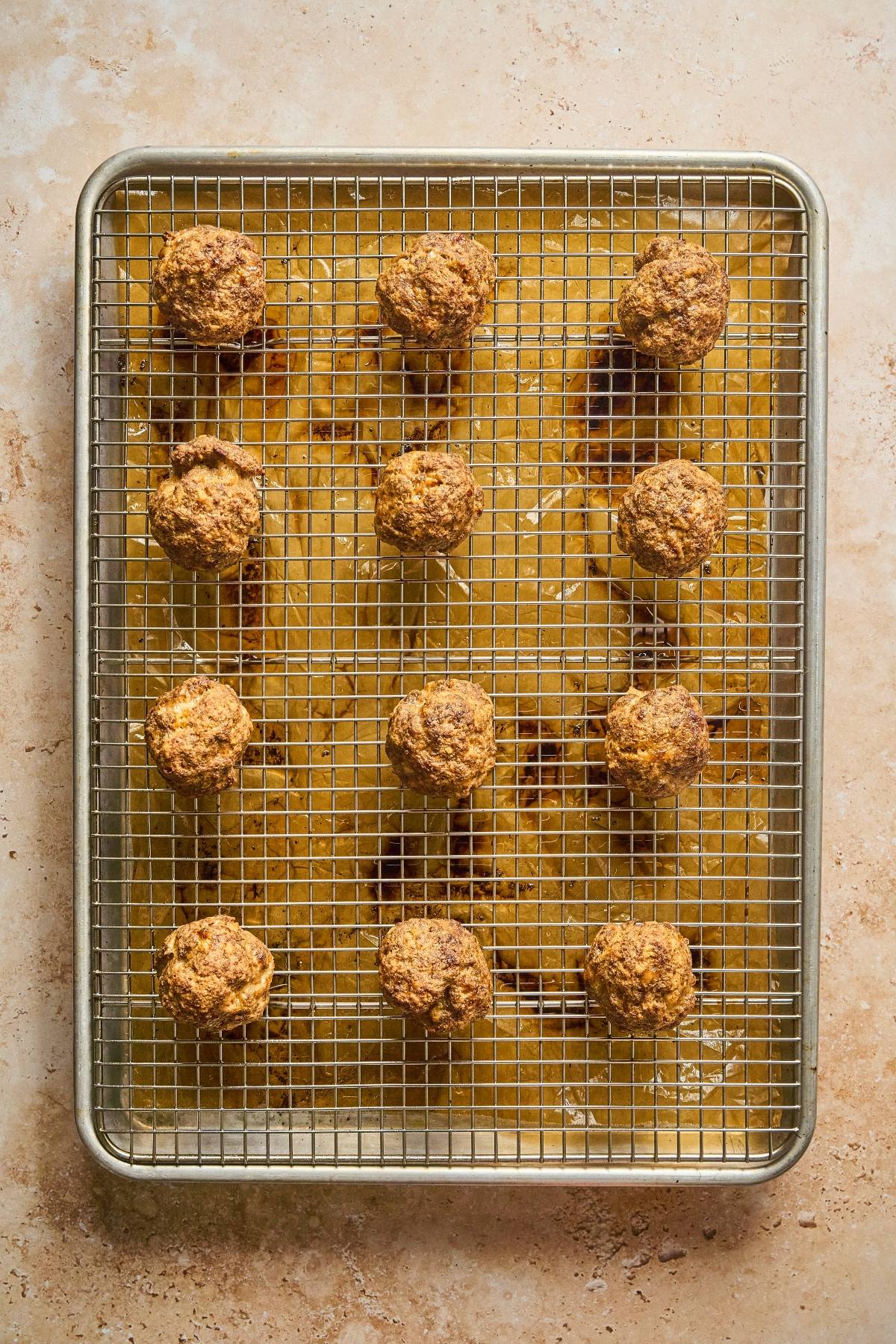 Twelve baked meatballs on a wire rack over a baking sheet, viewed from above.