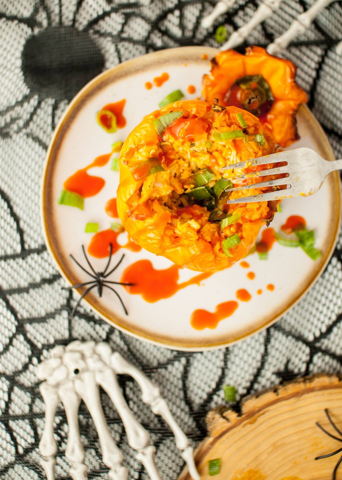 Stuffed orange bell pepper on a plate with hot sauce, green onions, and spooky Halloween decorations—perfect for jack o lantern peppers and creative Halloween party ideas for adults.