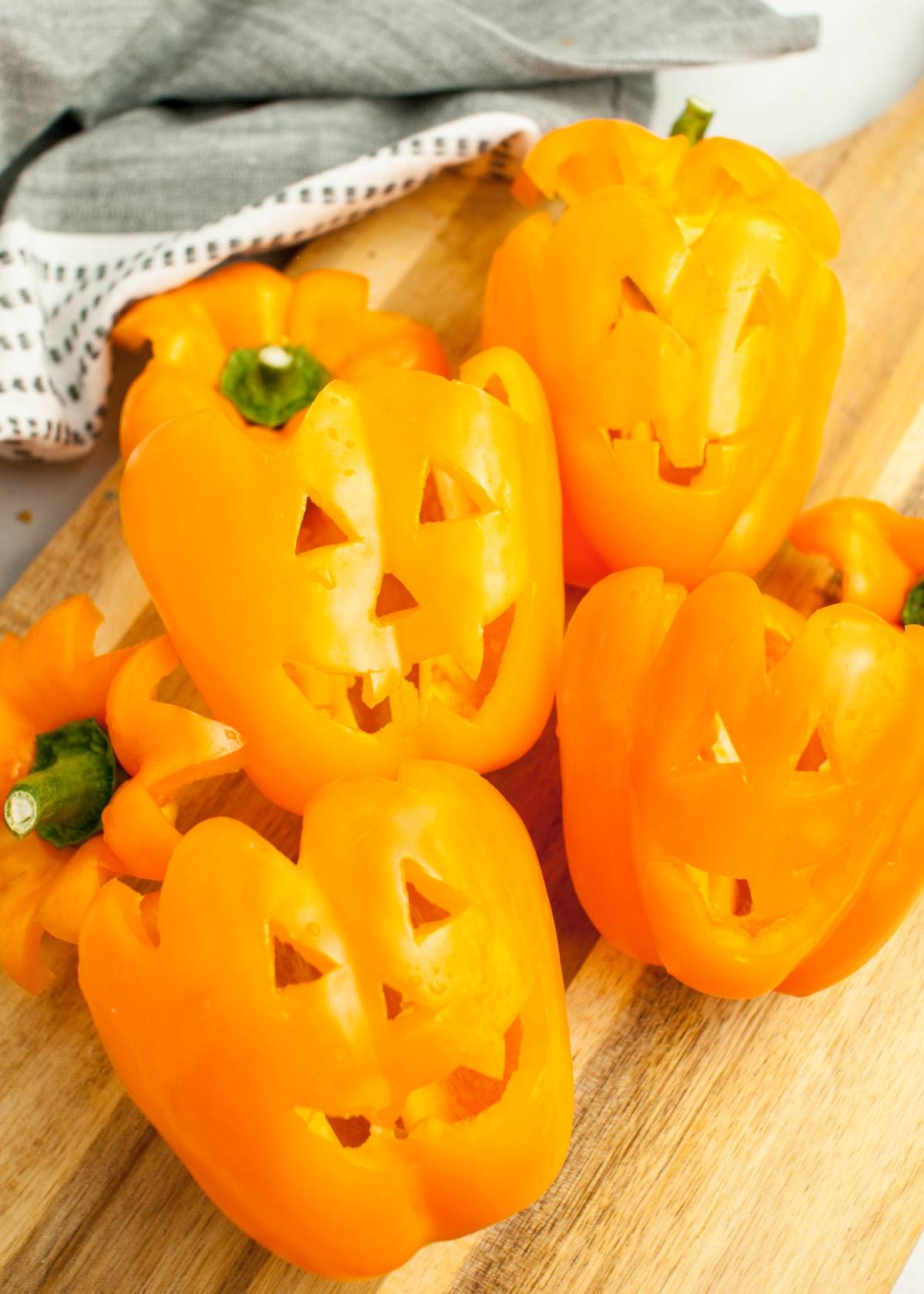 Four jack o lantern peppers, expertly carved with spooky faces, are arranged on a wooden surface—perfect as a creative Halloween dinner recipe or centerpiece for Halloween party ideas for adults.