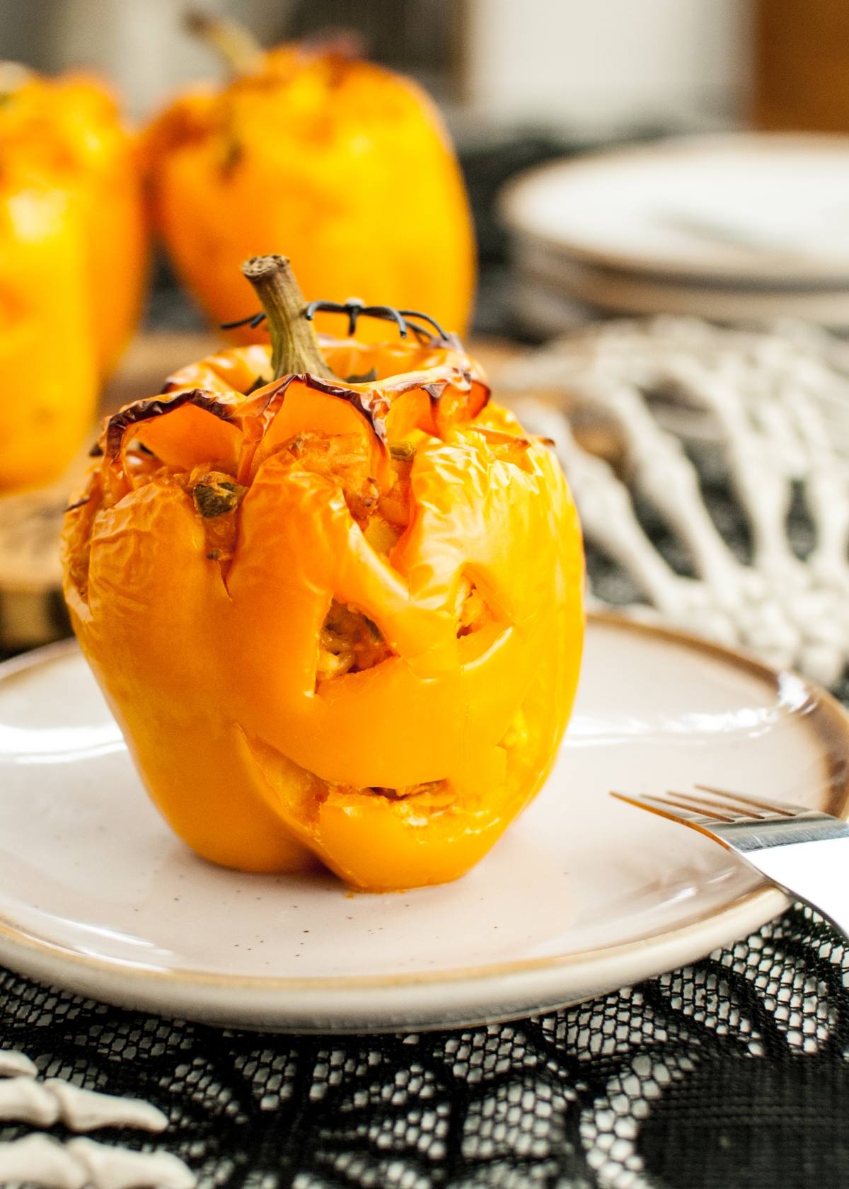 A yellow bell pepper carved like a jack-o'-lantern, stuffed and served on a white plate—a fun Jack-O-Lantern Stuffed Peppers idea for your next Halloween dinner recipe.