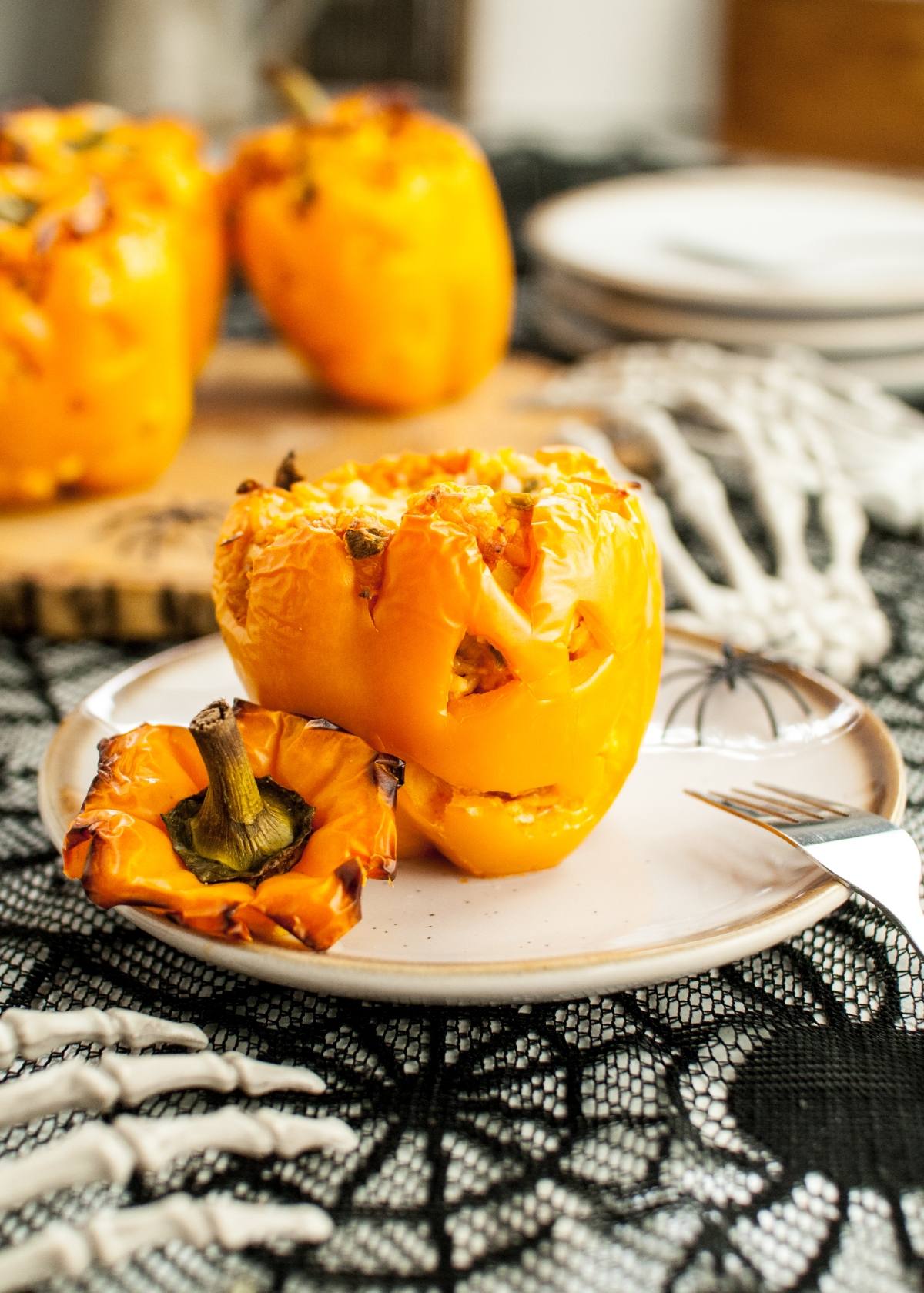 A yellow bell pepper carved like a jack-o'-lantern, served on a plate with a skeleton hand decoration—perfect Jack-O-Lantern Stuffed Peppers for creative food to eat on Halloween.