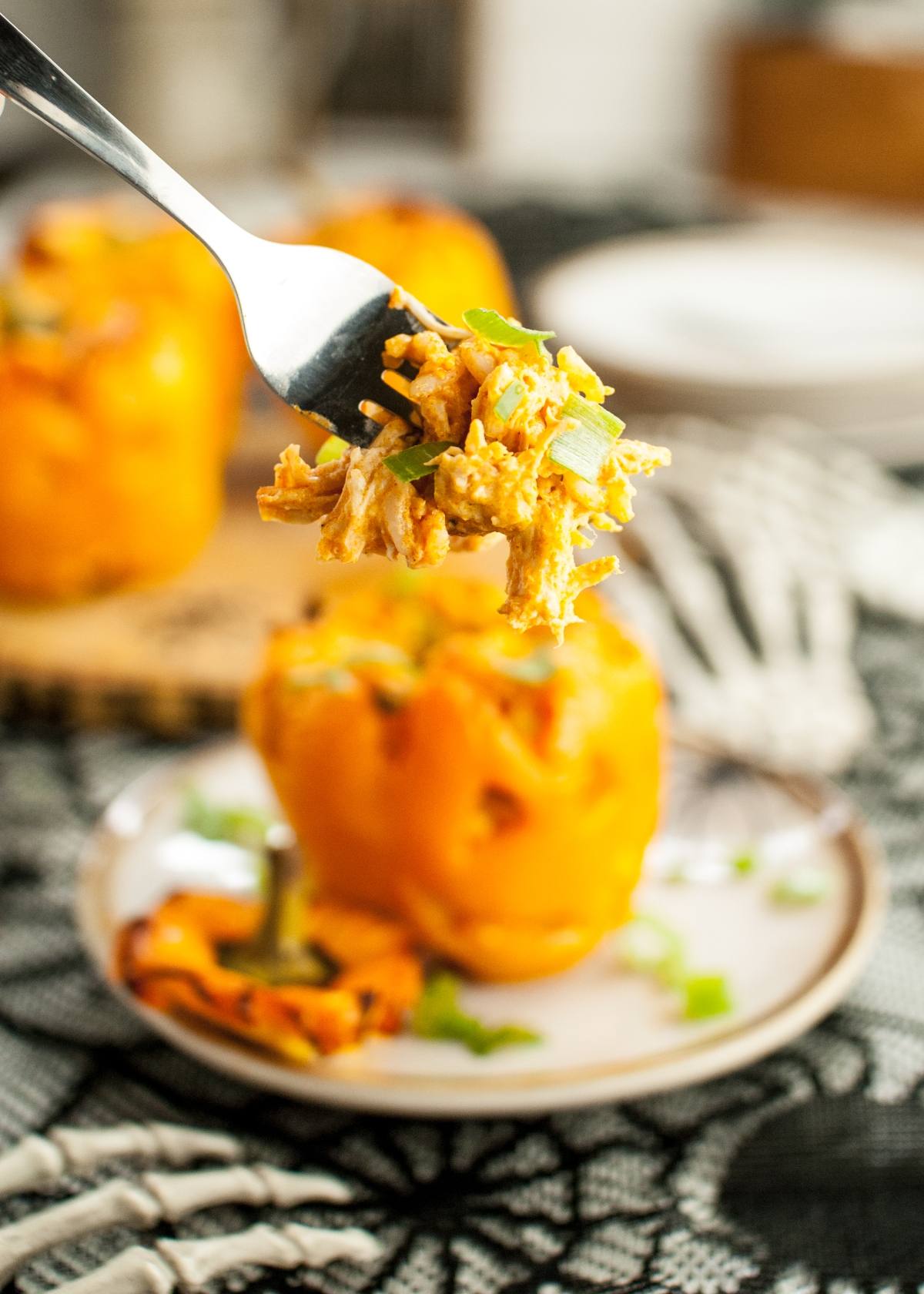 A fork holds a bite of stuffed orange bell pepper above a plate, with a skeleton hand fork beside it—a spooky touch perfect for your next Halloween dinner recipe.