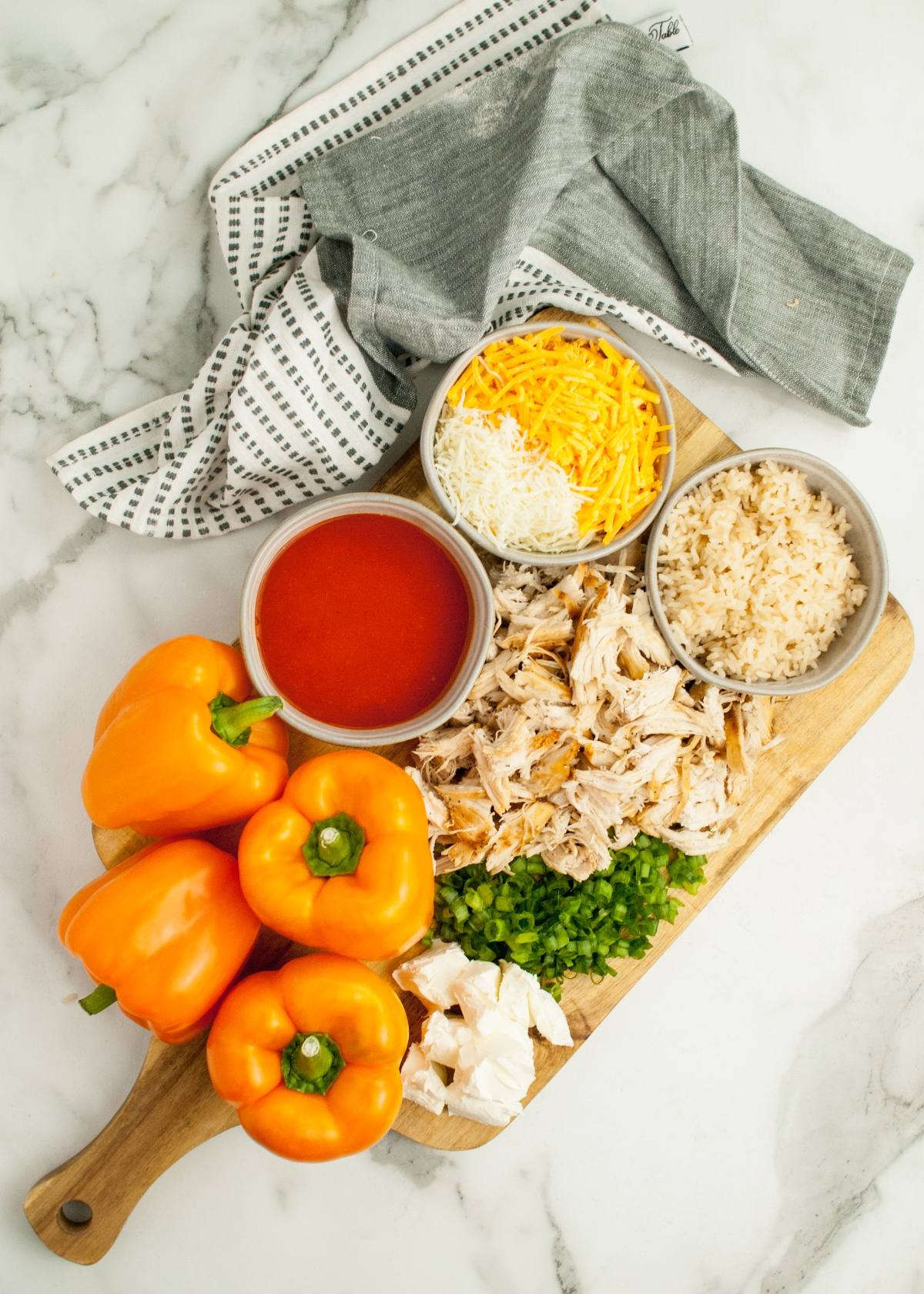 Chopped chicken, rice, cheese, tomato sauce, green onions, and orange bell peppers come together for a festive Halloween dinner recipe inspired by Jack-O-Lantern Stuffed Peppers. Served on a wooden board.