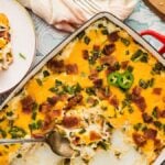 Jalapeño popper casserole topped with bacon and extra jalapeños, served with a spoon on a decorative table.