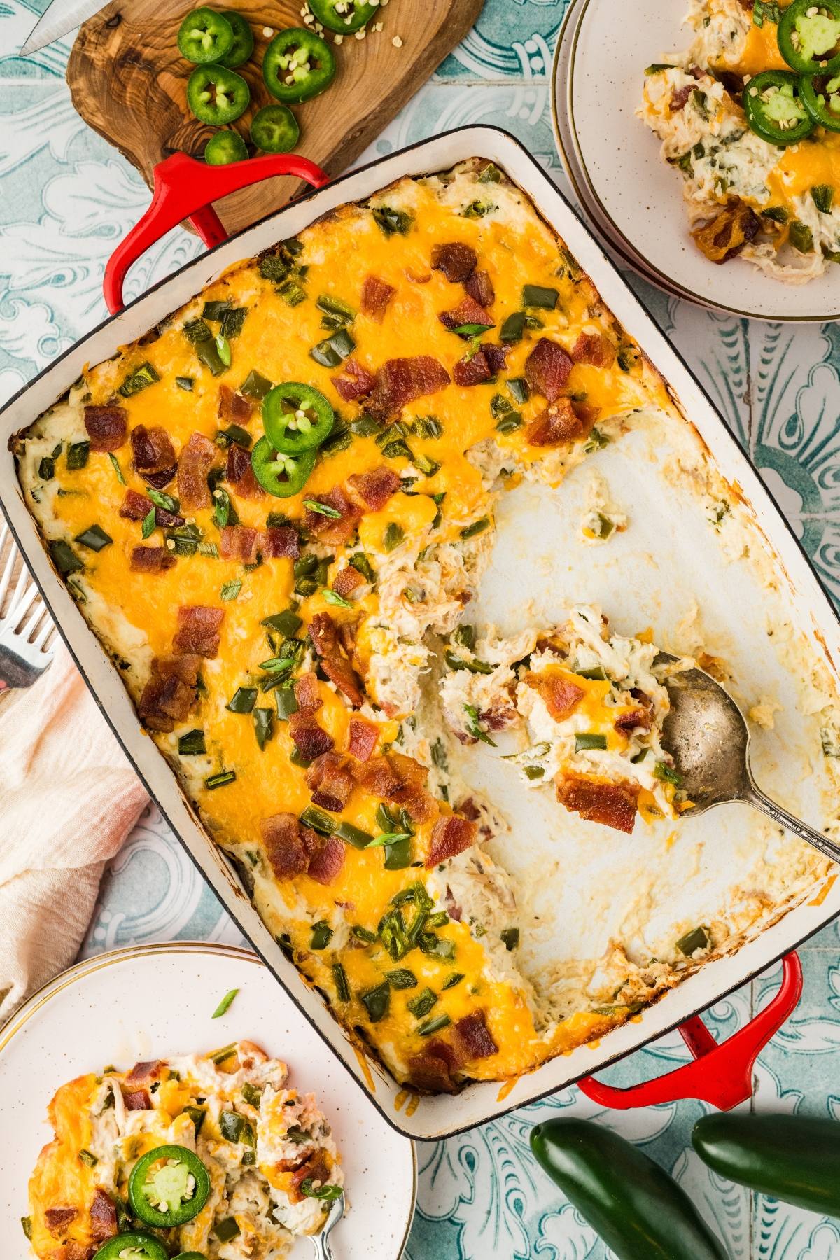 A casserole dish filled with cheesy, baked casserole topped with bacon, jalapeños, and chopped green onions.