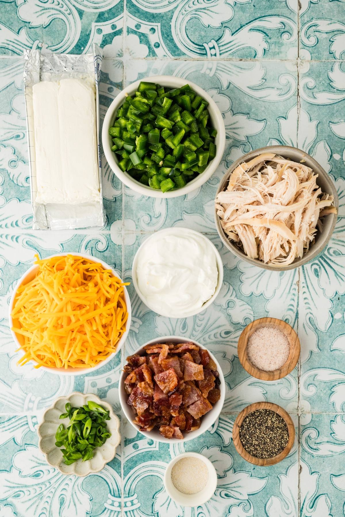 Bowls of chopped jalapeños, shredded chicken, cheddar cheese, bacon, cream cheese, sour cream, and seasonings.