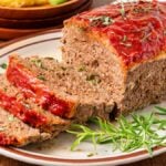 A sliced Lipton Meatloaf with tomato glaze on a plate, garnished with fresh rosemary.