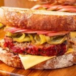 A hearty meatloaf sandwich with cheese, pickles, and crisp apple slices on rustic bread, served alongside crunchy potato chips.