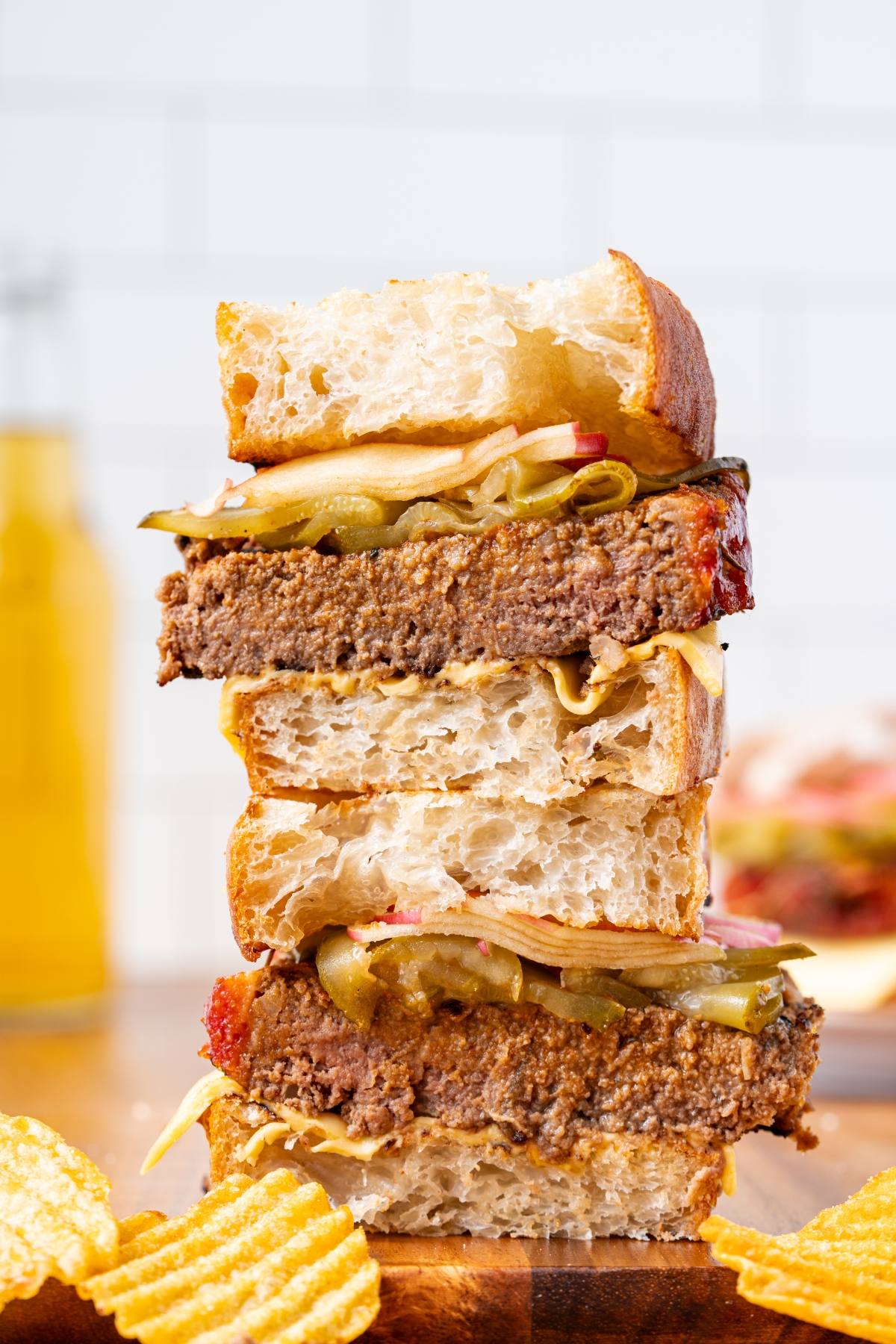 Stacked sandwich halves with thick bread, a veggie patty, pickles, and chips on the side.