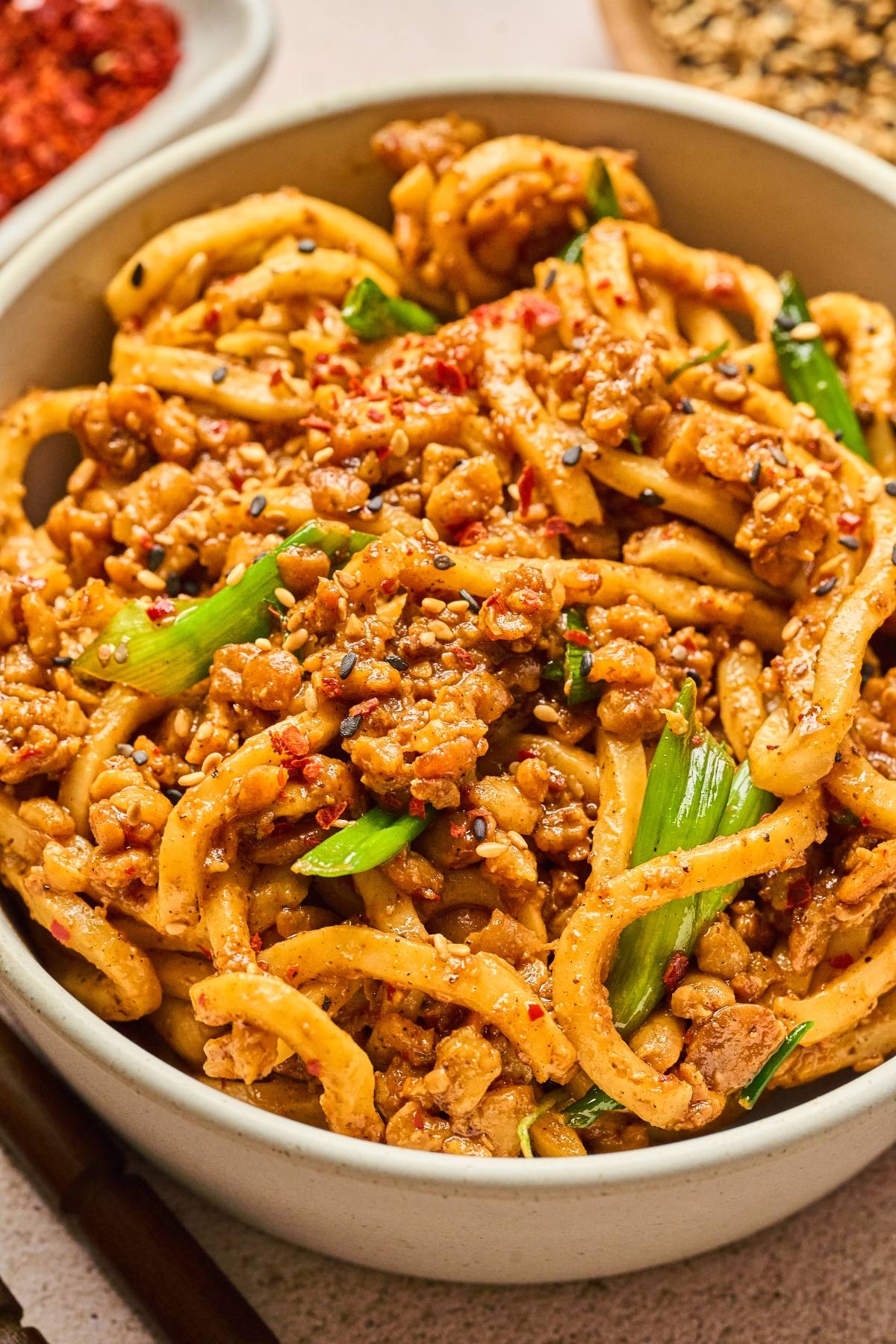 A bowl of spicy noodles with ground meat, green onions, and chili flakes.
