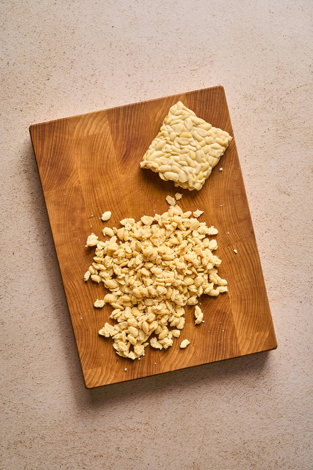 A block of tempeh and crumbled tempeh on a wooden cutting board.