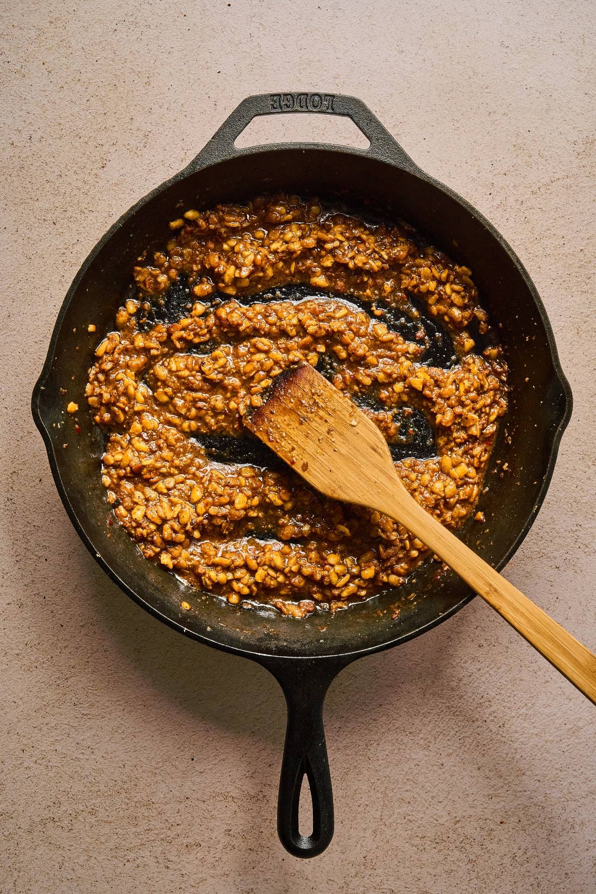 A cast iron skillet with a chunky sauce and a wooden spatula on a light countertop.