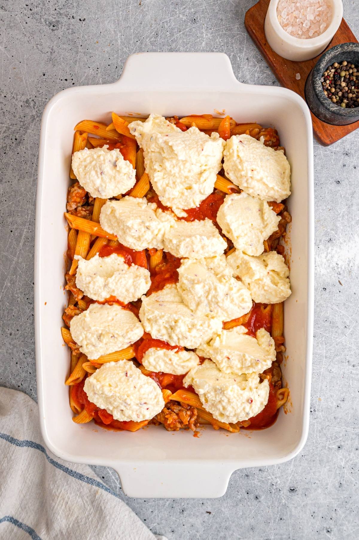 A baking dish of mostaccioli pasta with tomato sauce, ground meat, and dollops of ricotta cheese on top.