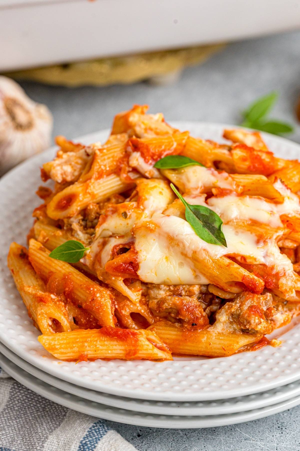 A plate of baked mostaccioli pasta with tomato sauce, melted cheese, ground meat, and fresh basil on top.
