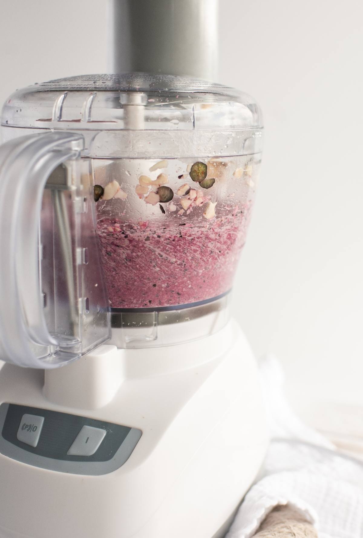 A food processor blending a pink smoothie with oats, seeds, and creamy goodness inside the container—made with raw cashews for a delicious raw vegan recipe.