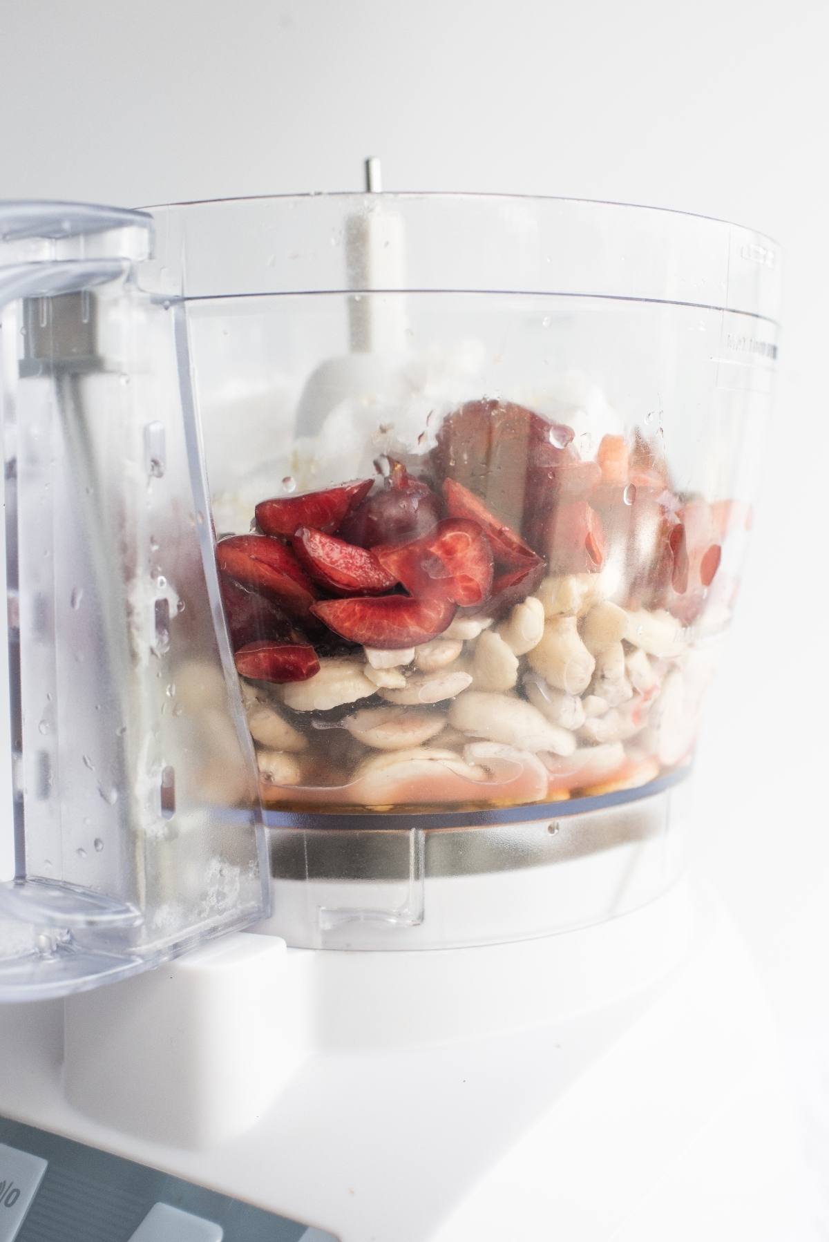 Sliced red bell peppers and white beans in a food processor bowl, ready to be blended for a delicious raw vegan recipe.