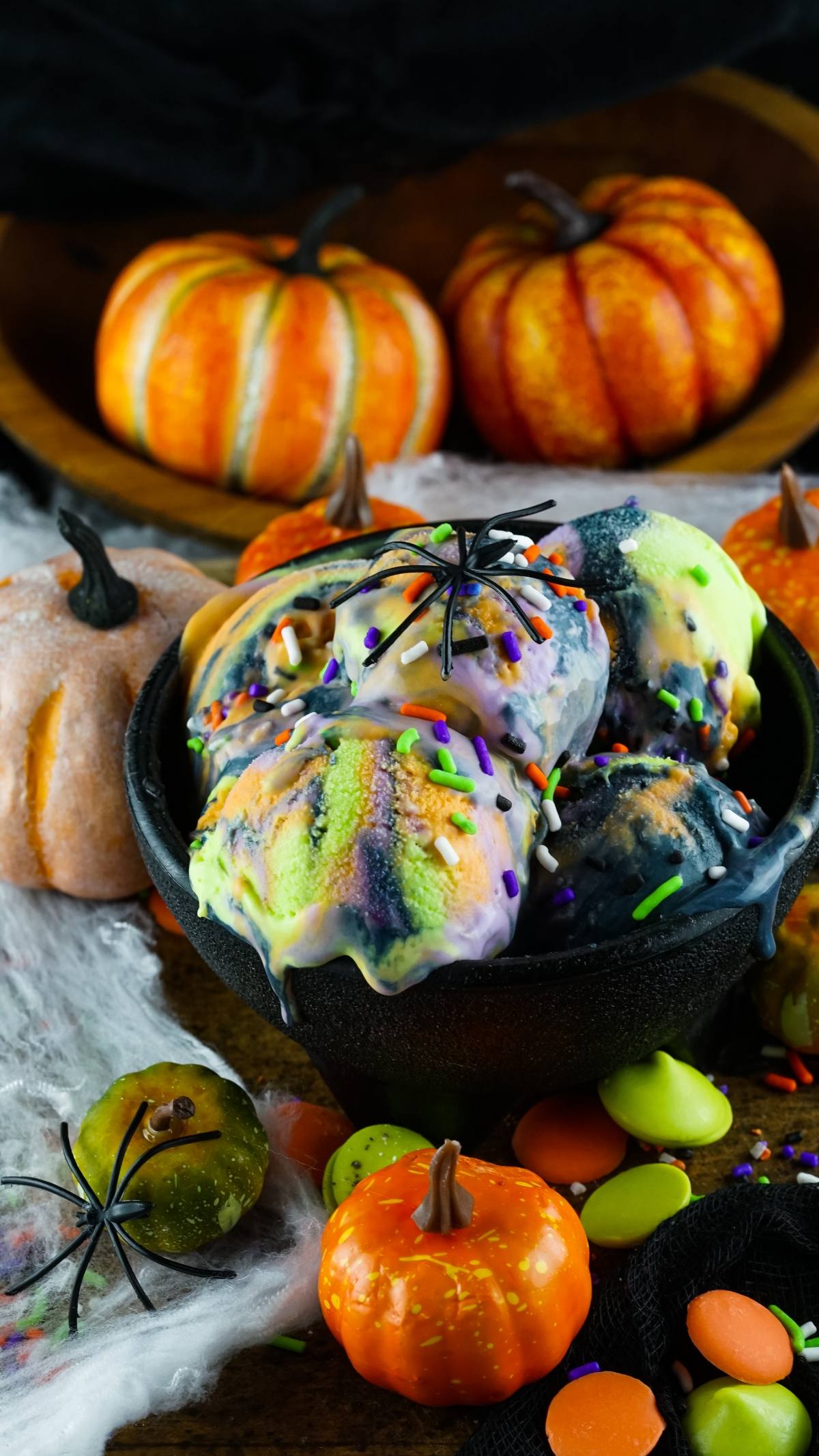 Scoops of birthday cake flavoured ice cream with Halloween sprinkles, toy spiders, and pumpkins in the background create a fun Dessert with Halloween colours.