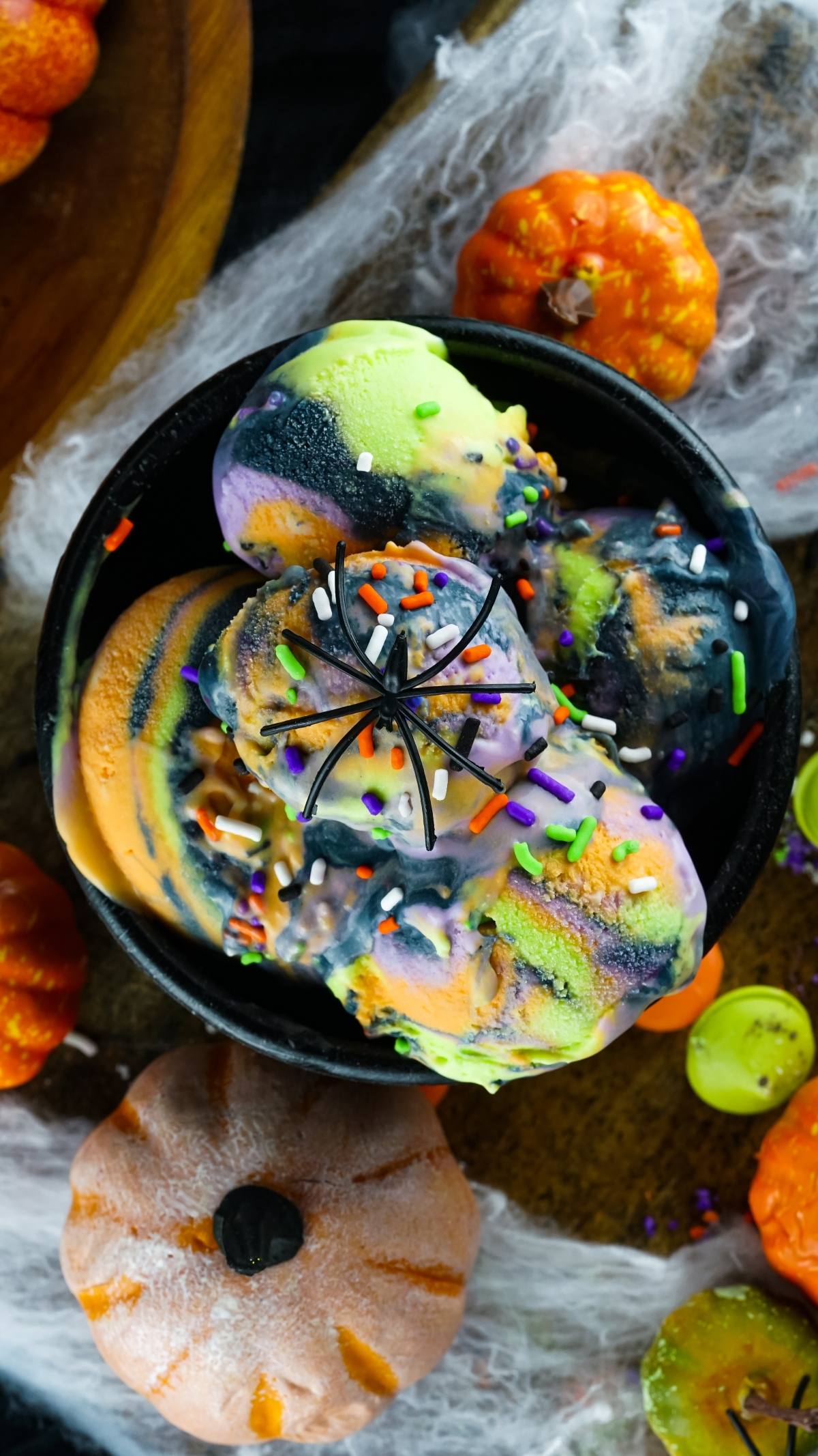 No Churn Halloween Ice Cream with orange, green, and purple swirls, birthday cake flavoured ice cream, topped with sprinkles and a fake spider—one of the best frozen Halloween treats for a spooky celebration.