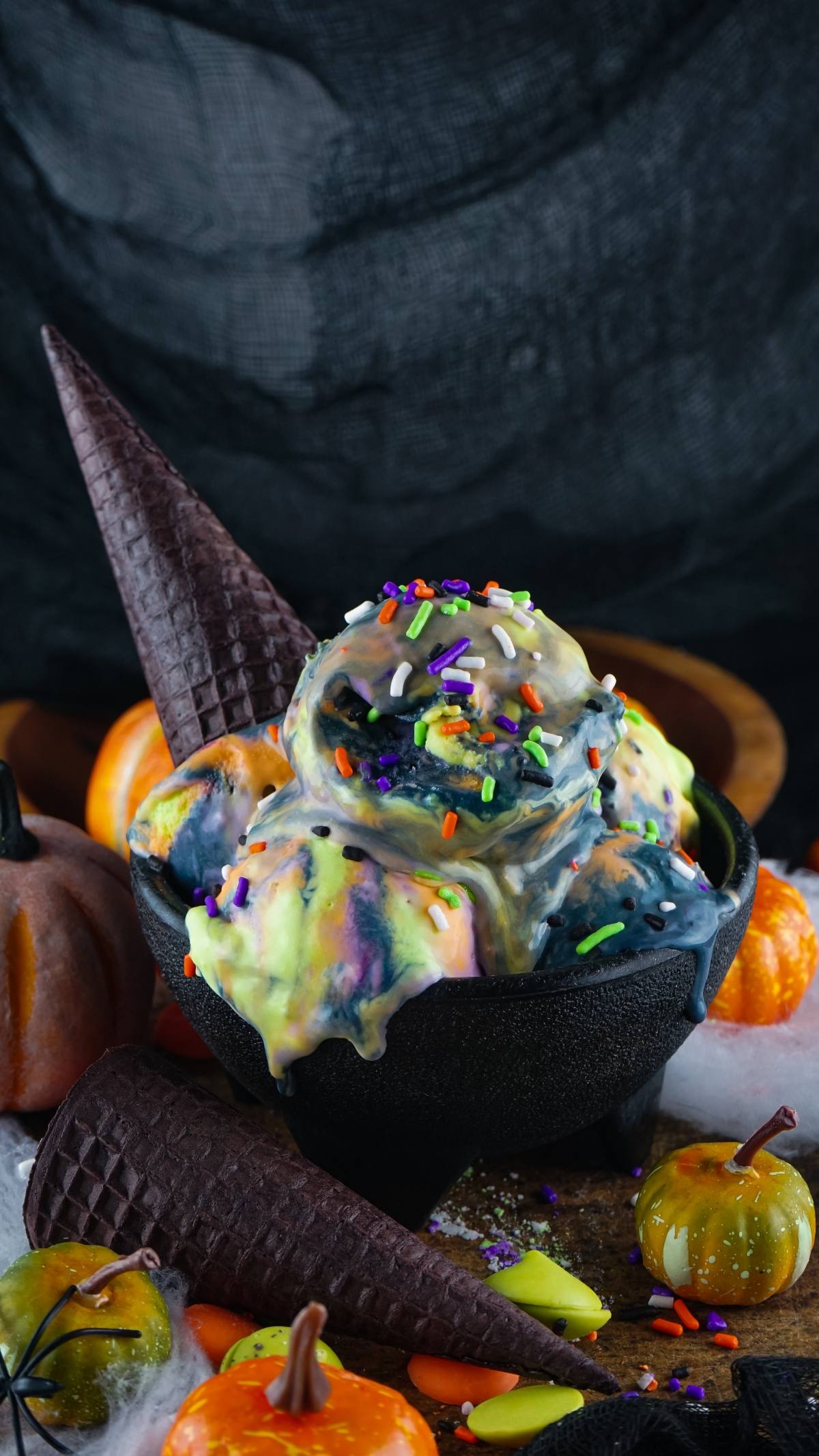 Spooky ice cream with colorful sprinkles served in a black bowl, surrounded by pumpkins and cones—this dessert with Halloween colours is the perfect festive treat.